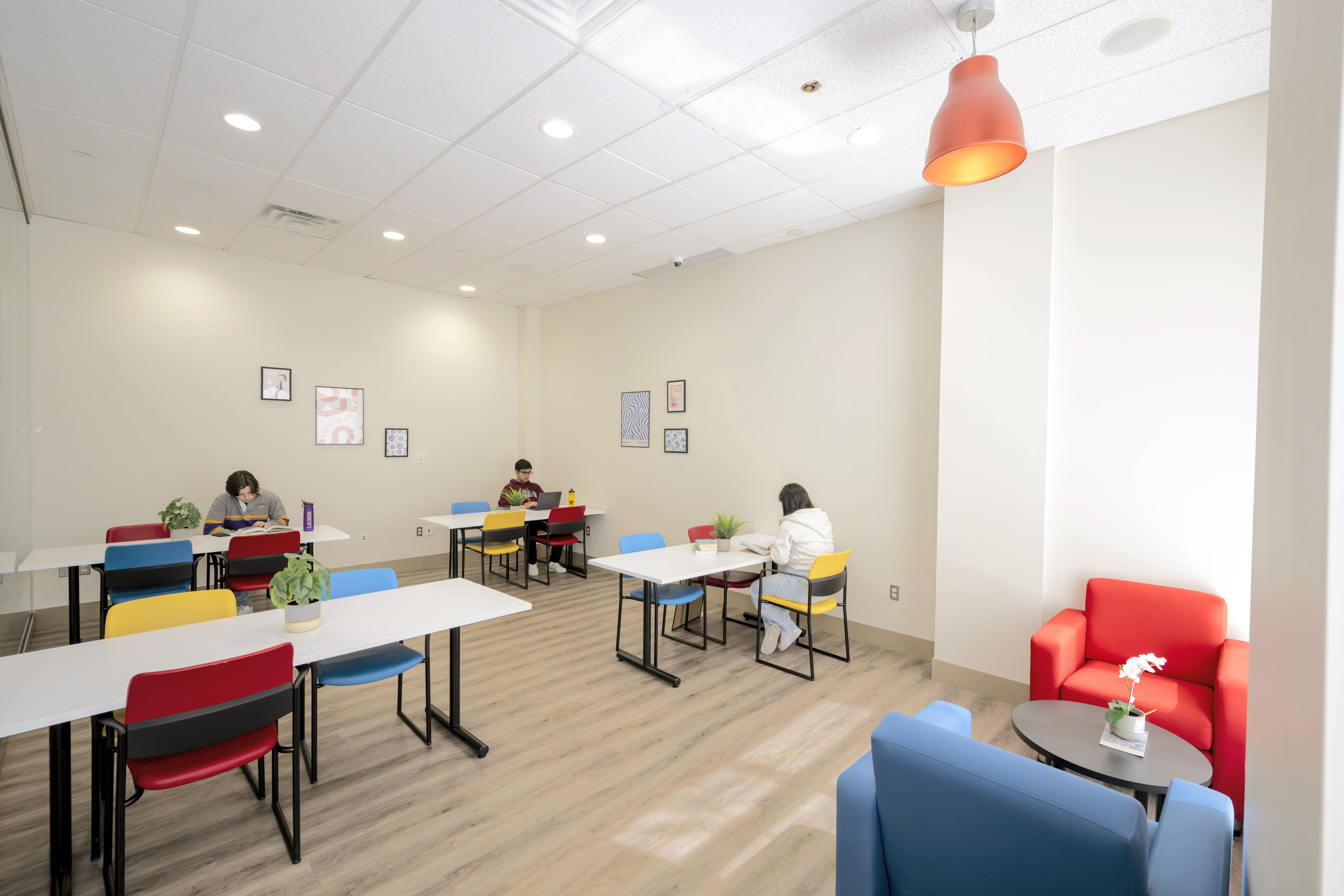Bright, modern study room with colorful chairs, sleek tables, and vibrant armchairs, offering a welcoming and collaborative environment.