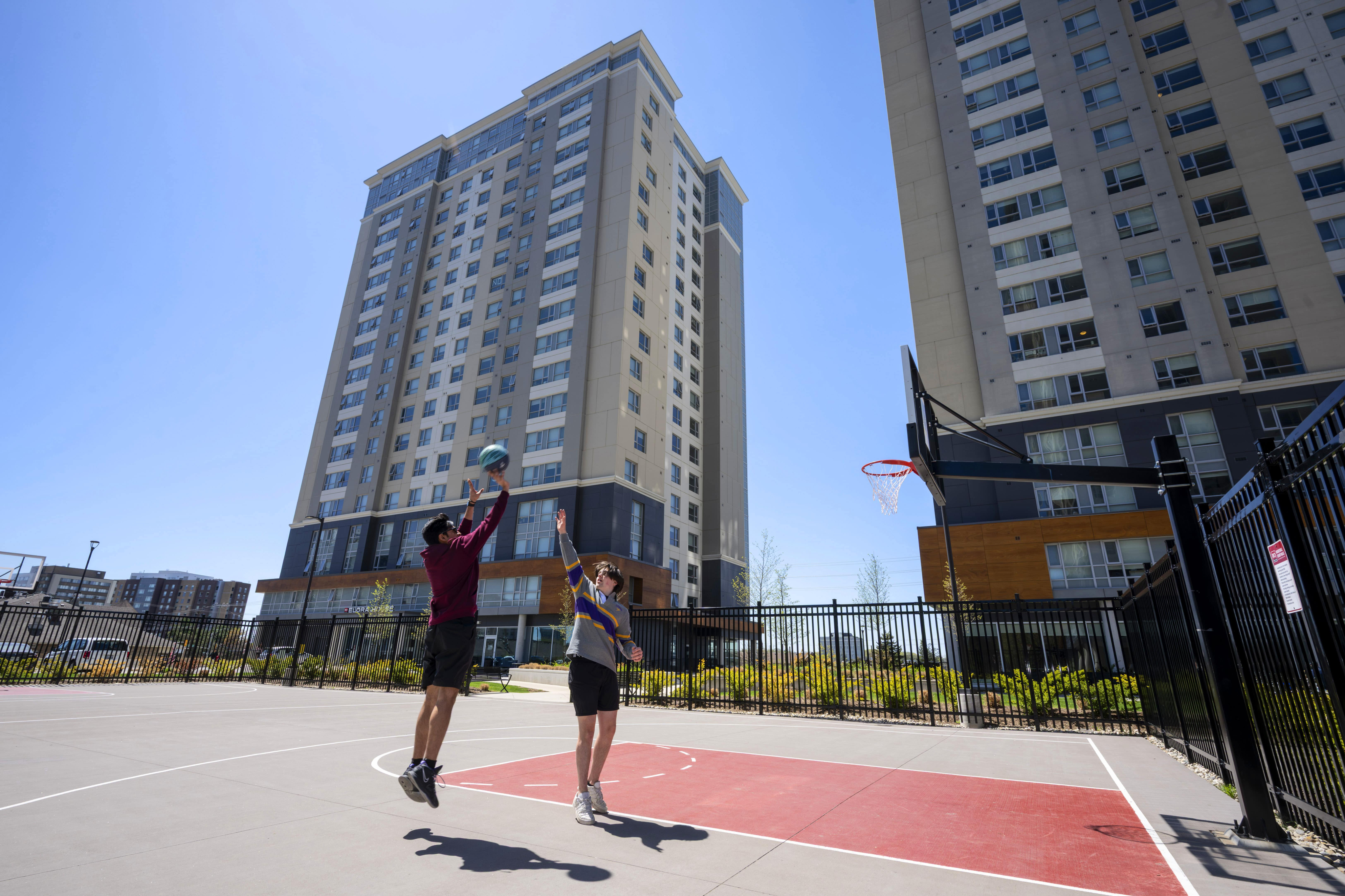 Vibrant urban apartment complex with modern high-rise buildings and an outdoor basketball court bathed in sunlight.