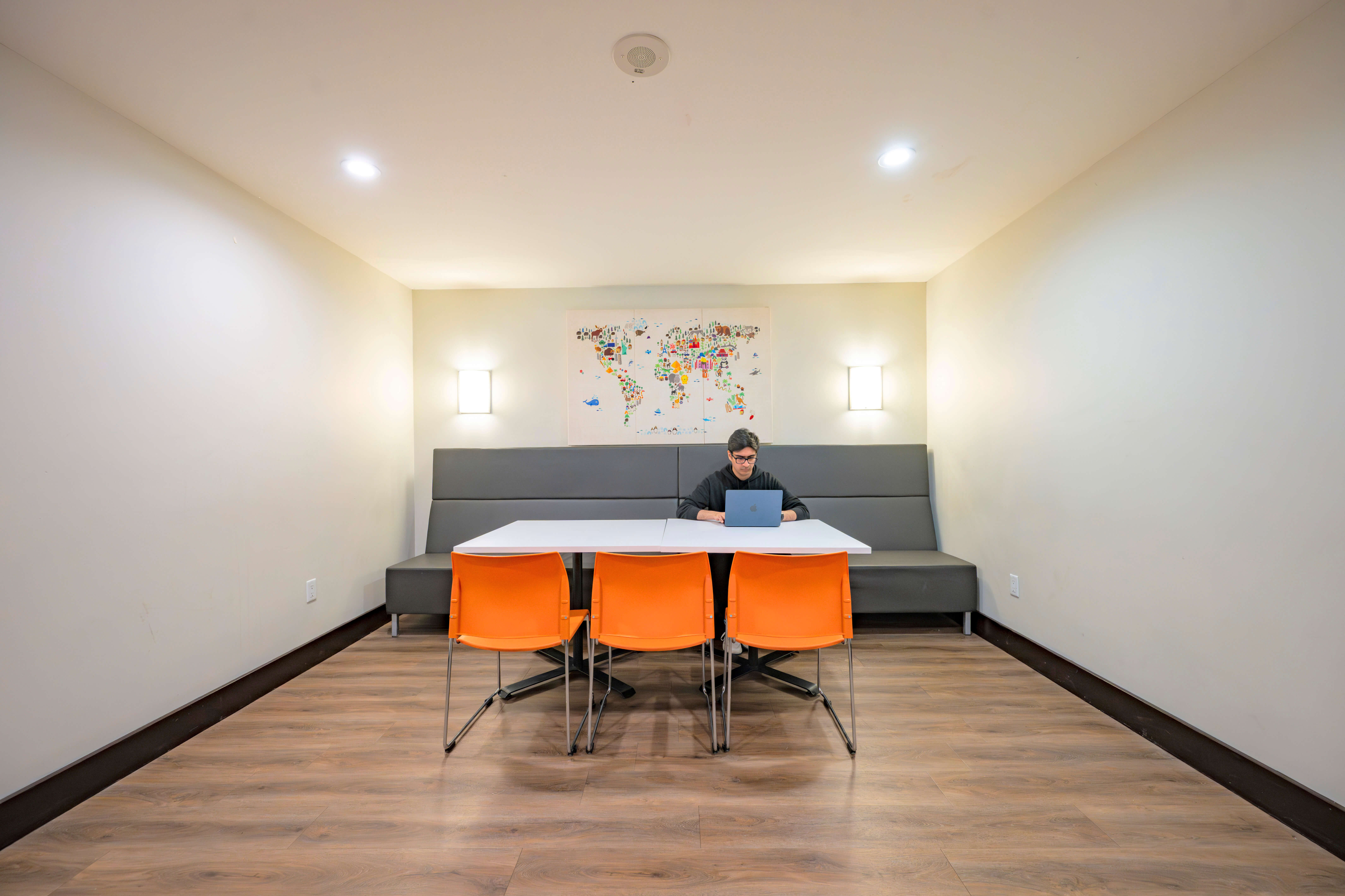 Inviting modern meeting area with a sleek white table, vibrant orange chairs, and world map art on the wall, perfect for creative brainstorming sessions.
