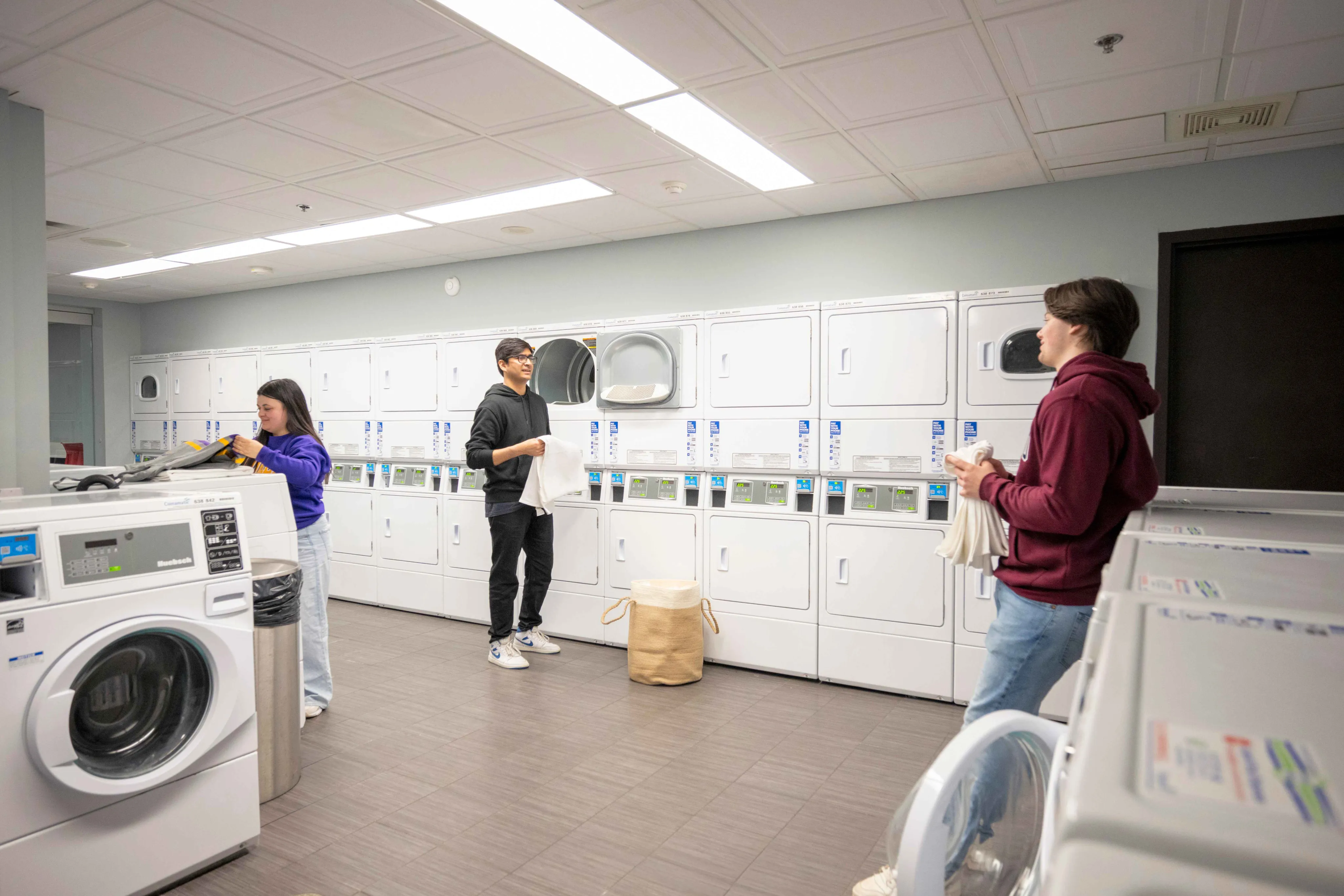 Modern laundry room with multiple washers and dryers, stylish lighting, and people enjoying a convenient communal space.