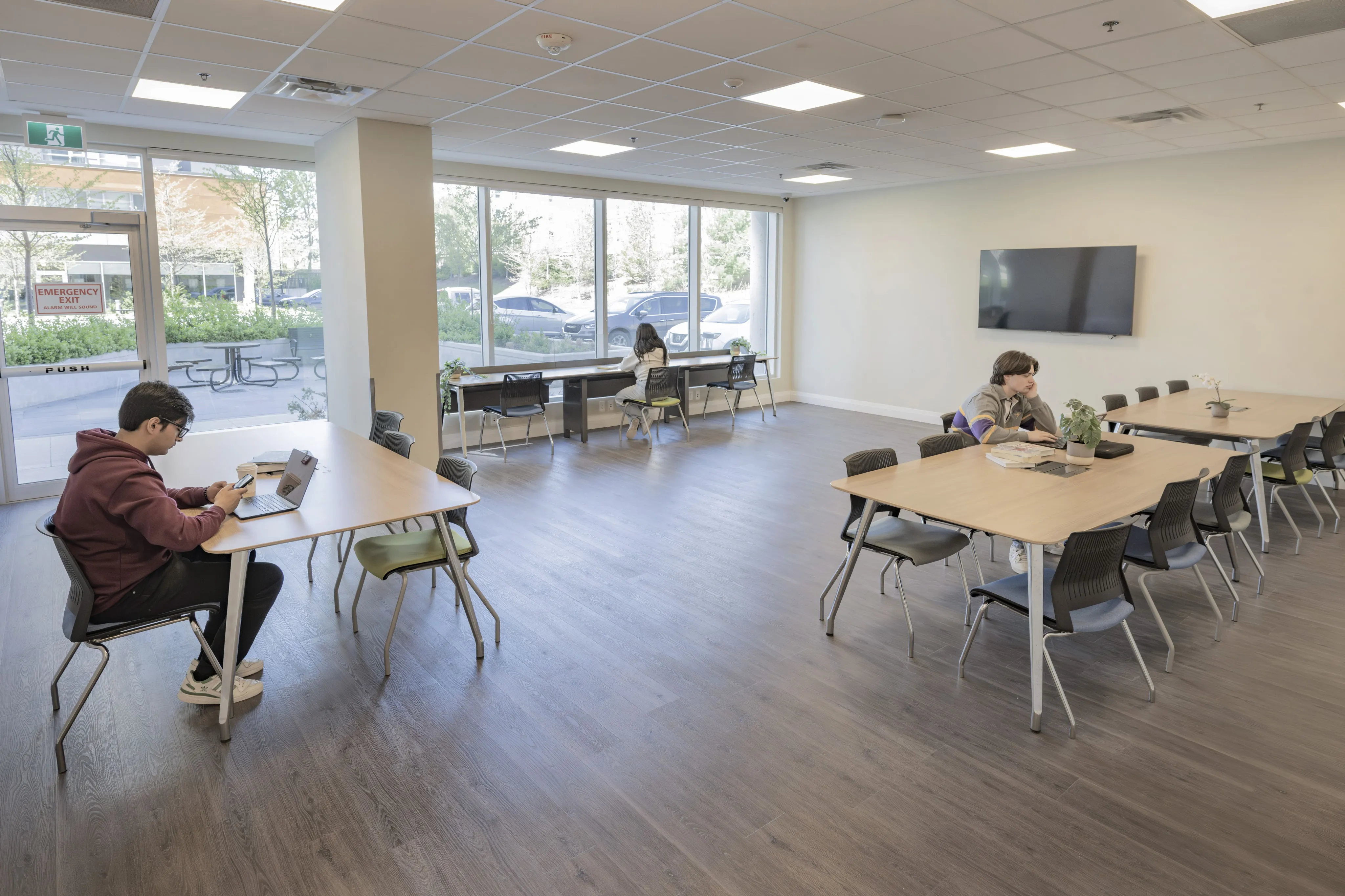 Bright, spacious community room with large windows, modern tables, and comfortable seating, ideal for studying or social gatherings.