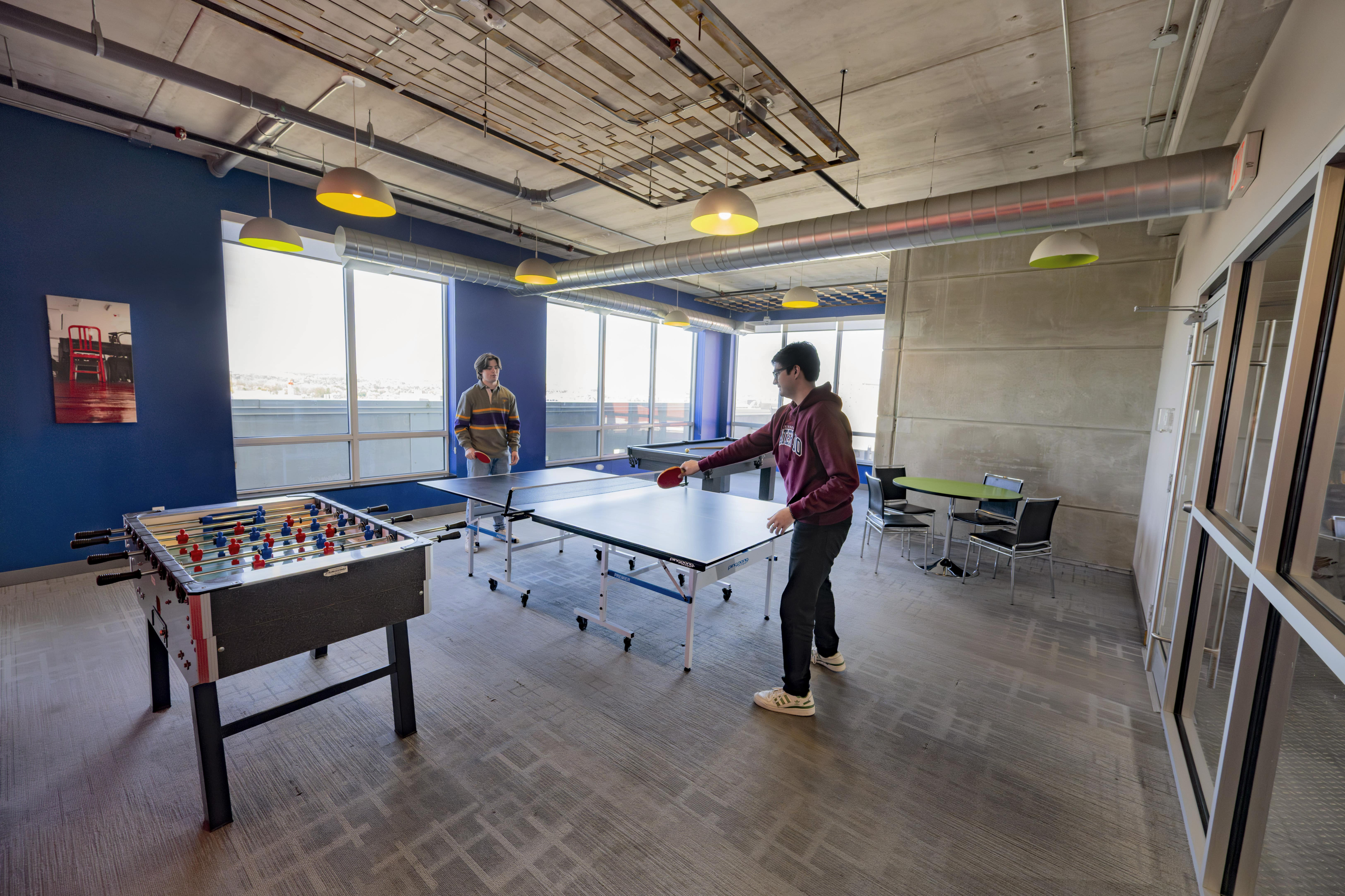 Vibrant recreational room featuring natural lighting with a ping pong table, foosball table, and stylish lounge seating.
