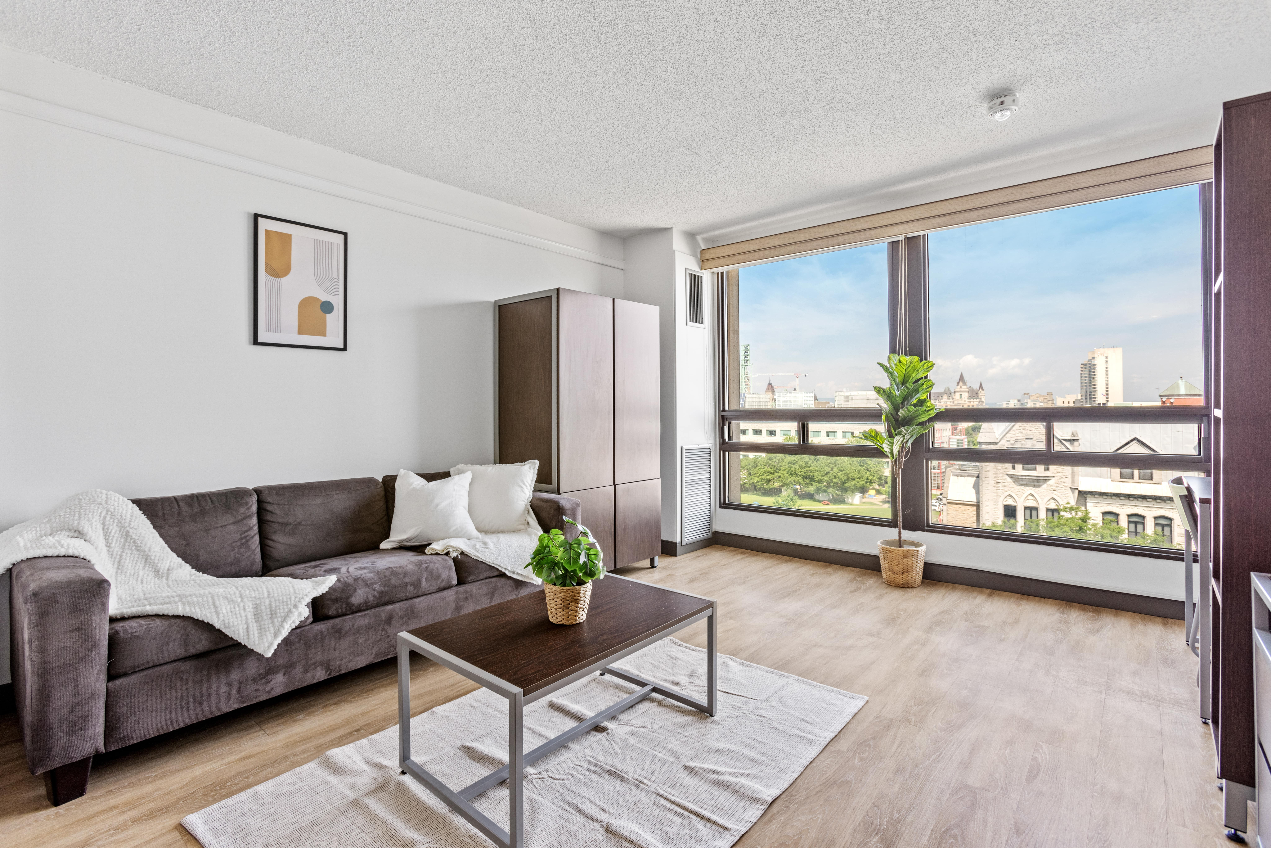 Bright living room with a modern sofa, elegant coffee table, and expansive city view through large windows.