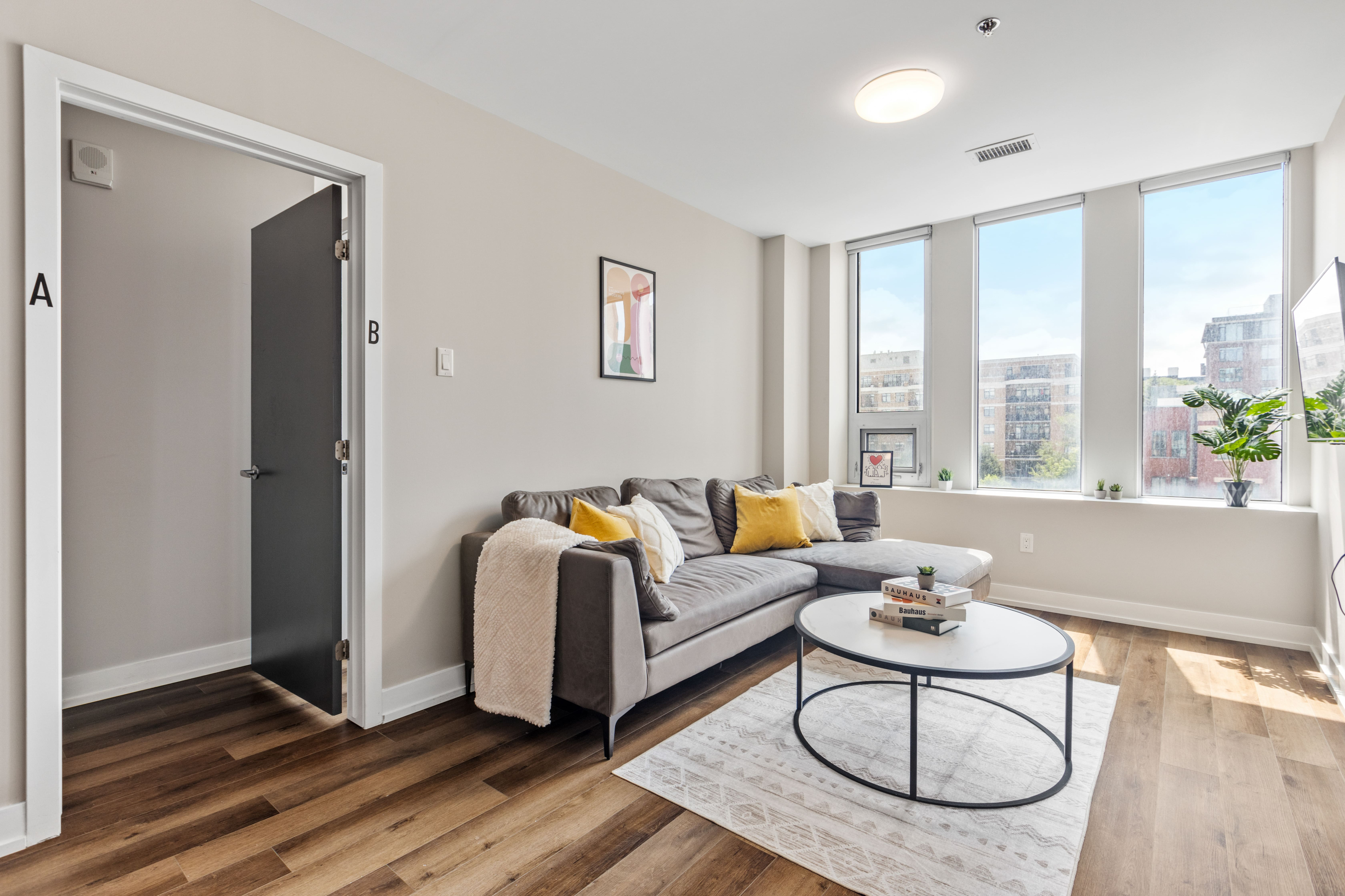 Bright and inviting living room featuring a modern gray sofa with yellow pillows, a stylish round coffee table, and expansive windows offering abundant natural light and city views.
