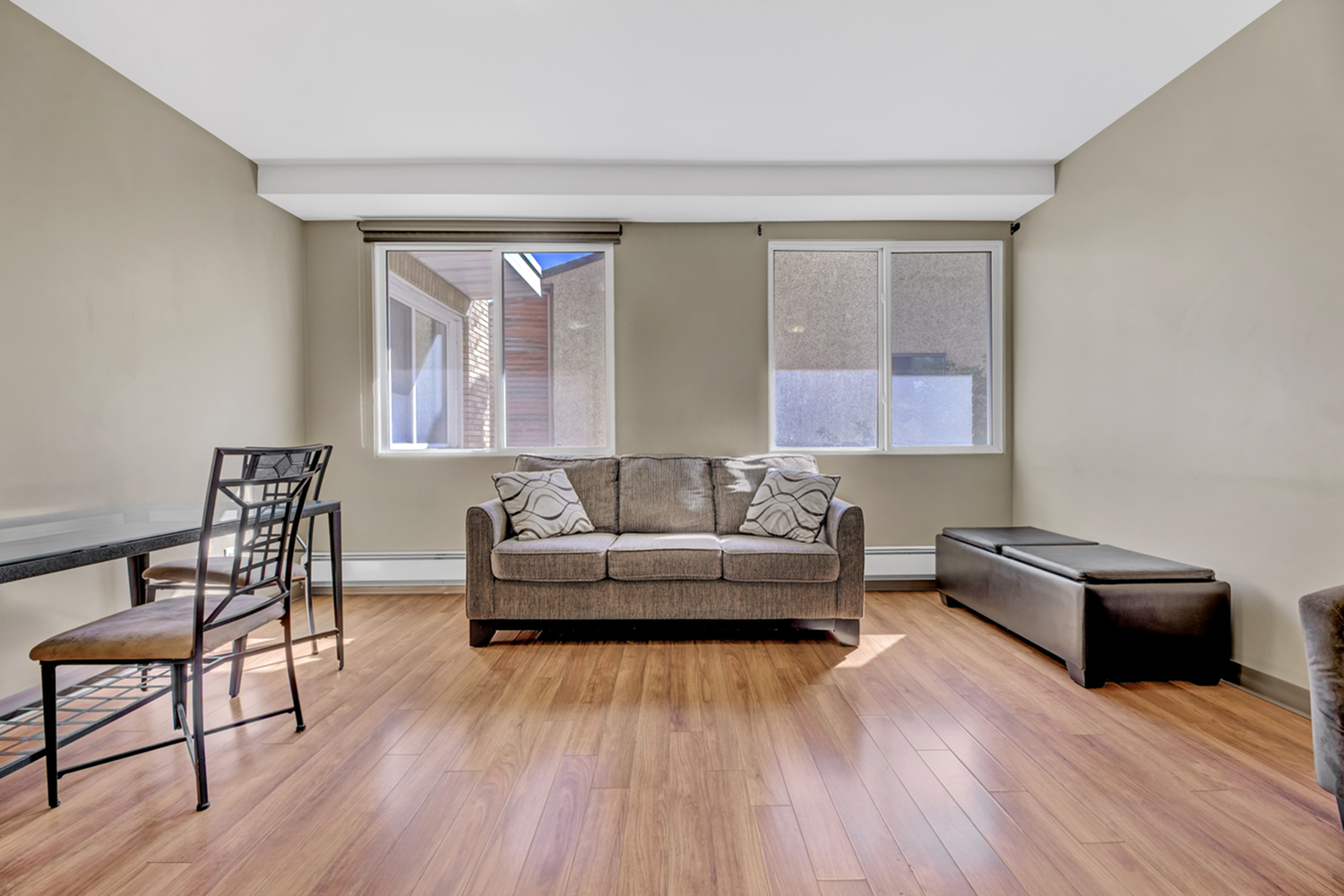 Bright living room with modern decor, featuring a cozy sofa, elegant wooden flooring, and large windows for natural light.