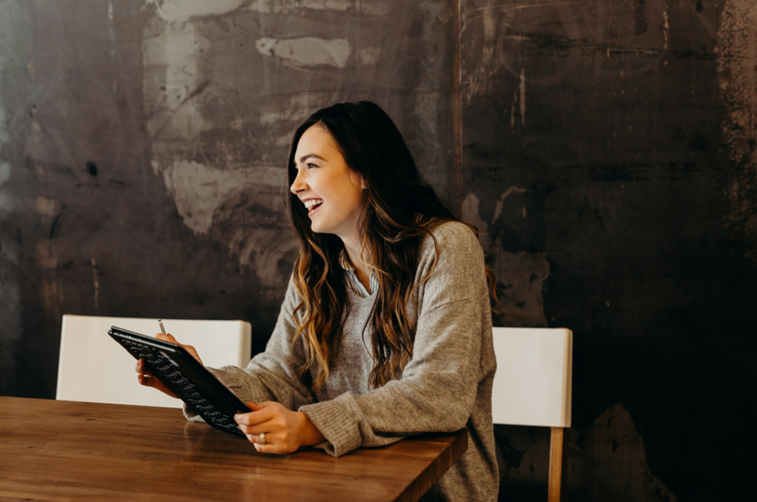 Cheerful person with long hair using a tablet in a cozy, modern setting, exuding positivity and engagement.