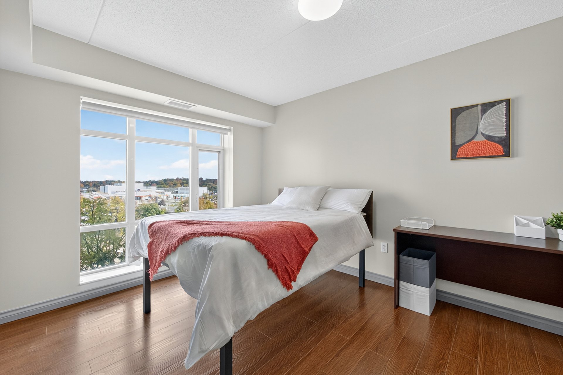 Bright and inviting bedroom with large windows revealing a scenic outdoor view, complemented by elegant wooden flooring and modern decor.