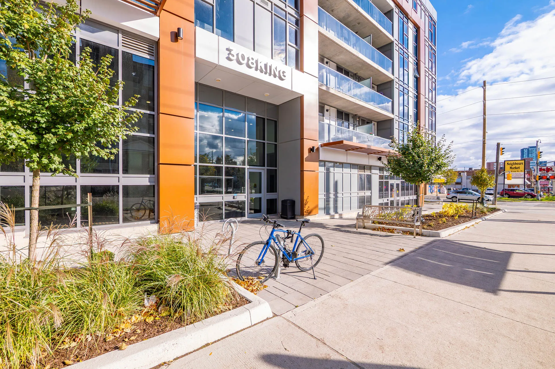 Modern apartment building with sleek glass windows, vibrant orange accents, and a welcoming entrance in a bustling neighborhood.