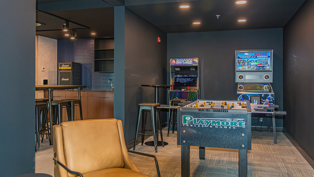 Vibrant recreation room featuring classic arcade games, sleek bar area, and a stylish foosball table, perfect for entertaining and relaxation.