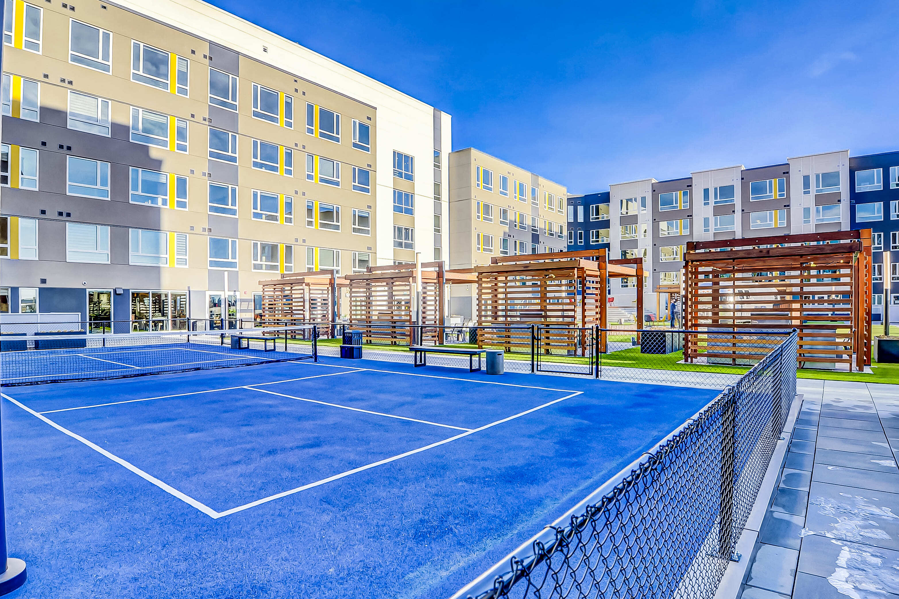 Modern apartment complex showcasing vibrant blue tennis court, stylish outdoor seating, and contemporary architecture.