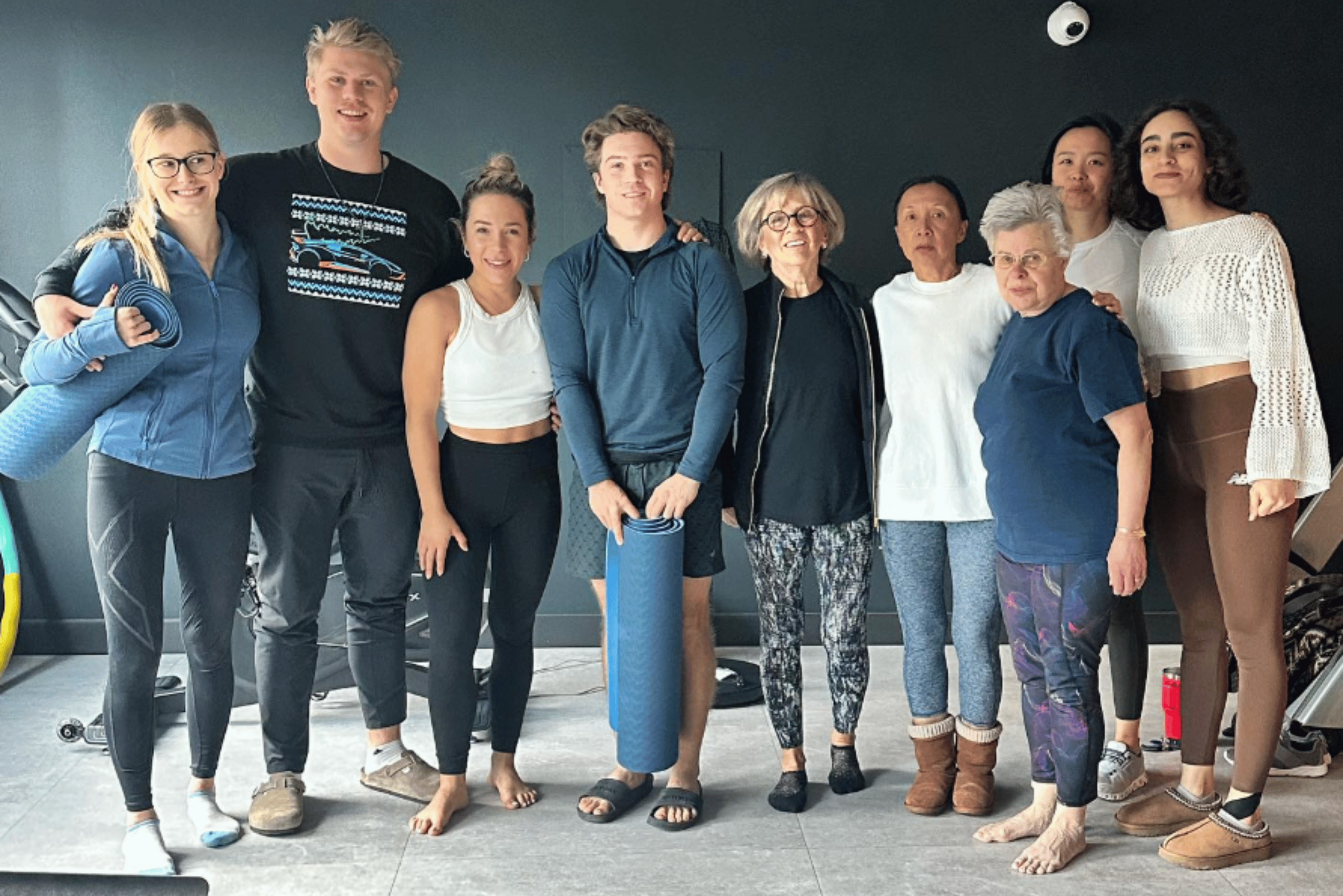 Diverse group of people smiling and holding yoga mats in a modern fitness studio environment.
