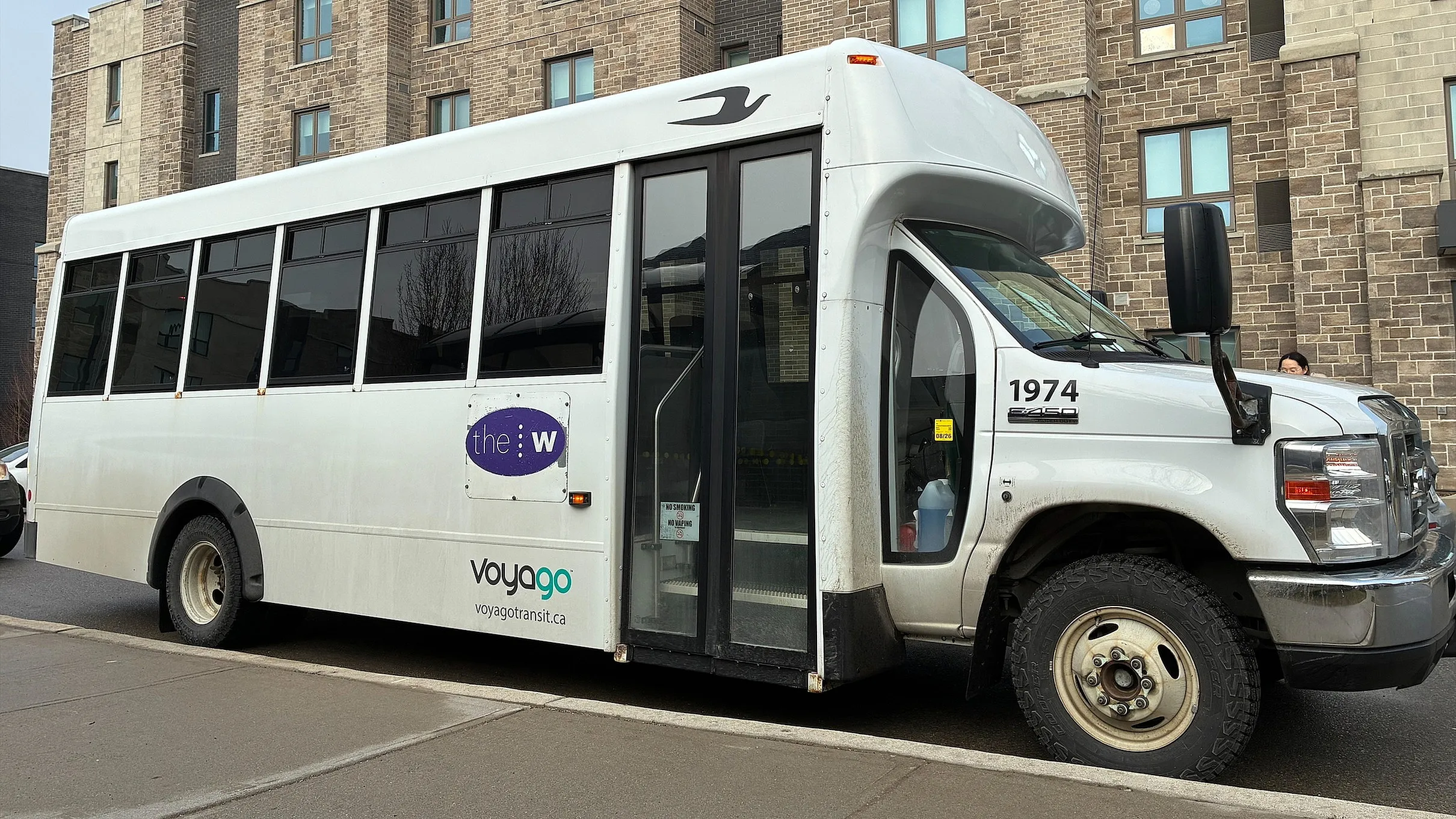 Modern shuttle bus parked in front of a contemporary brick apartment building, showcasing convenient transportation options for residents.