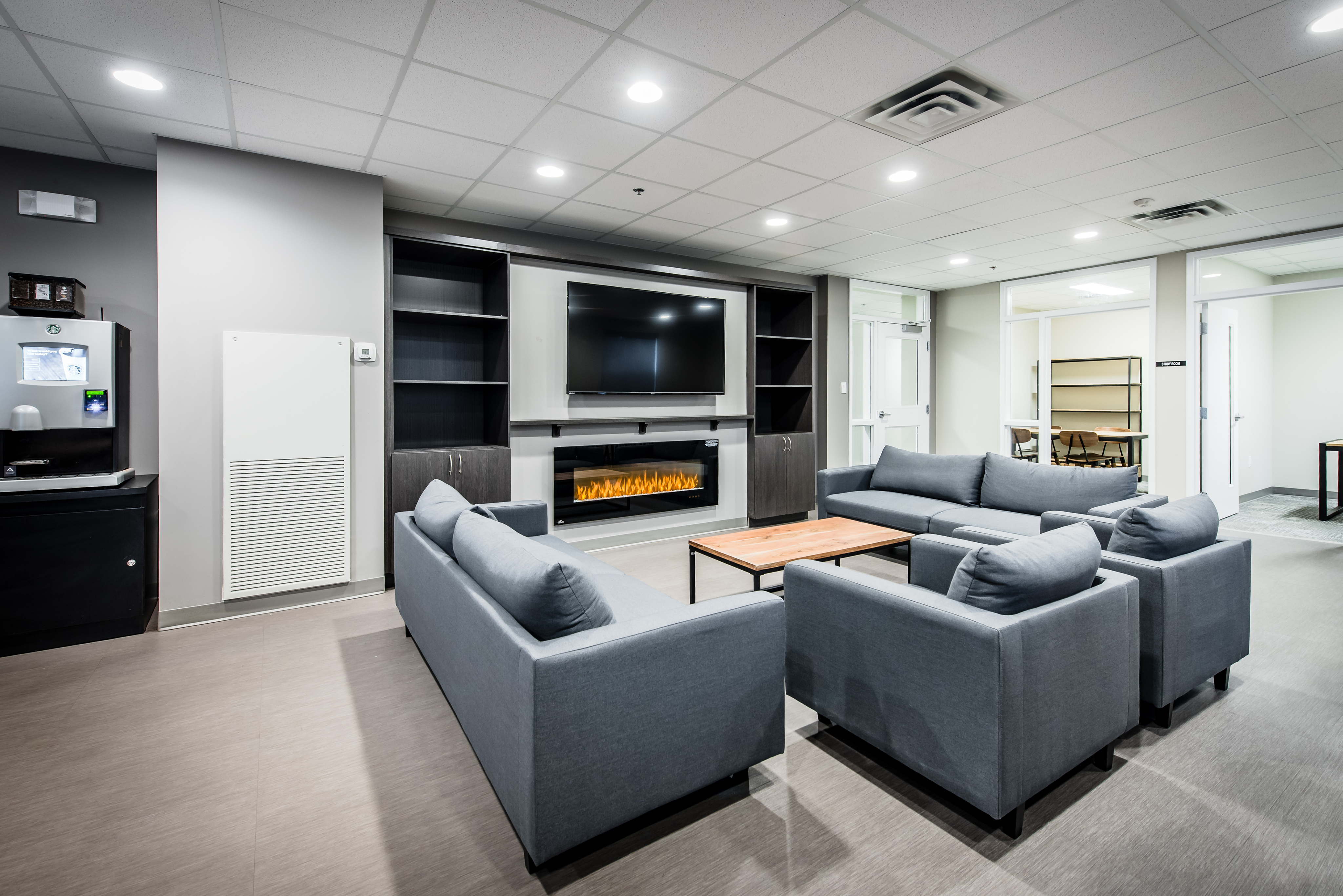 Modern lounge area with sleek gray sofas, a flat-screen TV, and a cozy electric fireplace, perfect for relaxation and entertainment.