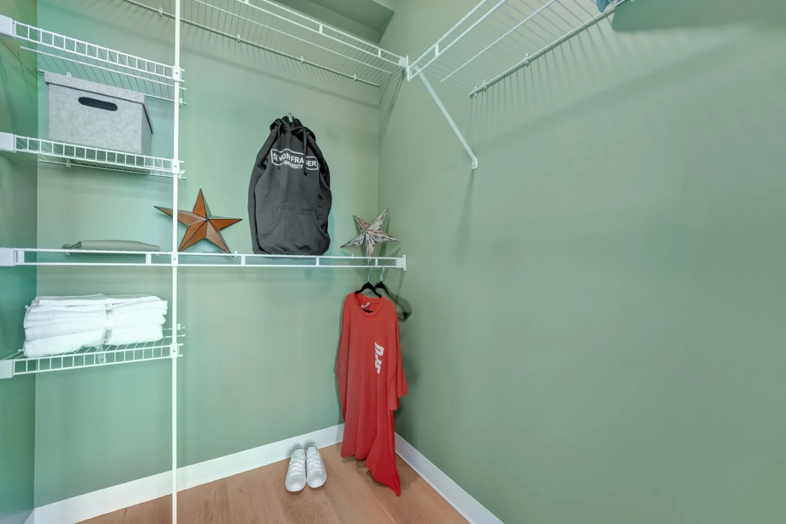 Luxurious walk-in closet with ample shelving and storage space, featuring soft green walls and elegant hardwood flooring.
