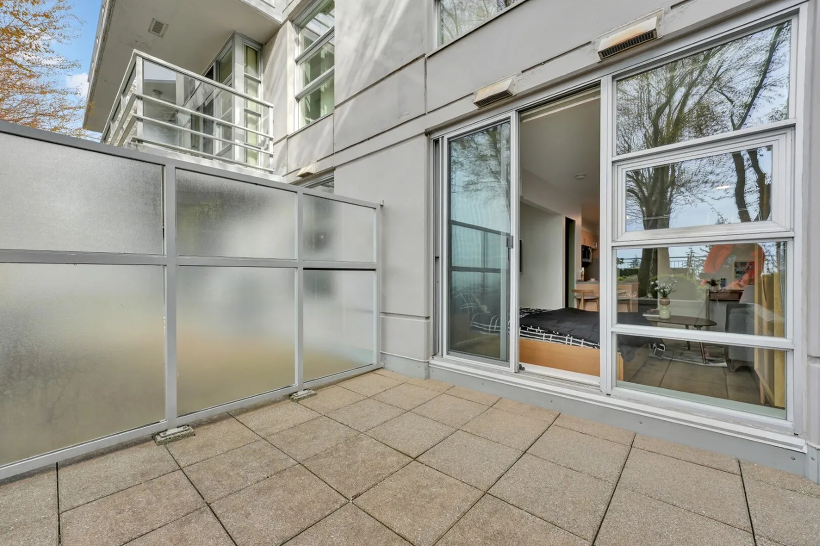 Modern apartment featuring a cozy bedroom with sliding glass doors opening to a private, sunlit patio with frosted privacy panels.