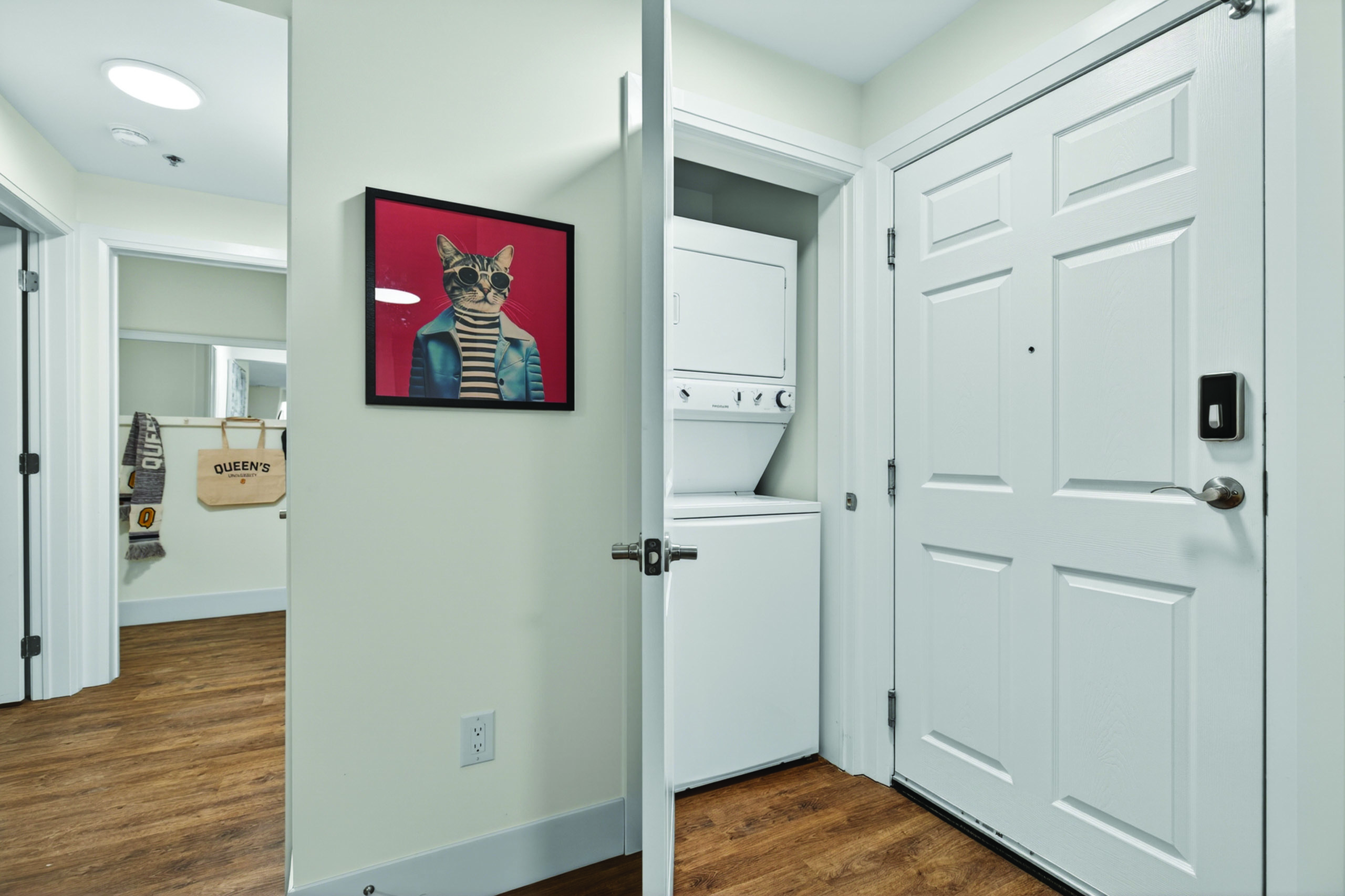 Chic apartment entrance showcasing in-unit laundry, modern wood flooring, and playful cat artwork.