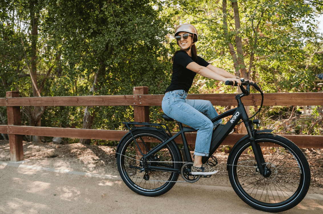 Woman enjoying a sunny day riding a modern black bicycle on a scenic outdoor path.