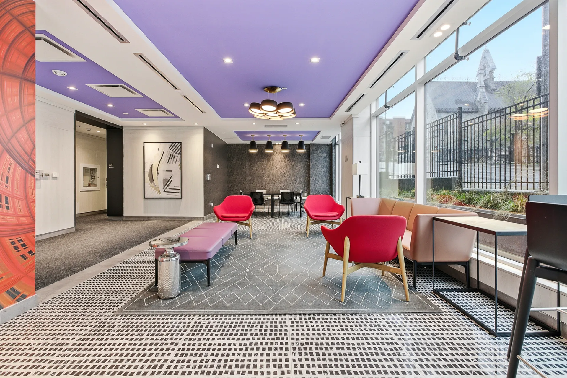 Vibrant and modern lounge area with bold red chairs, chic lighting, and expansive windows letting in natural light.