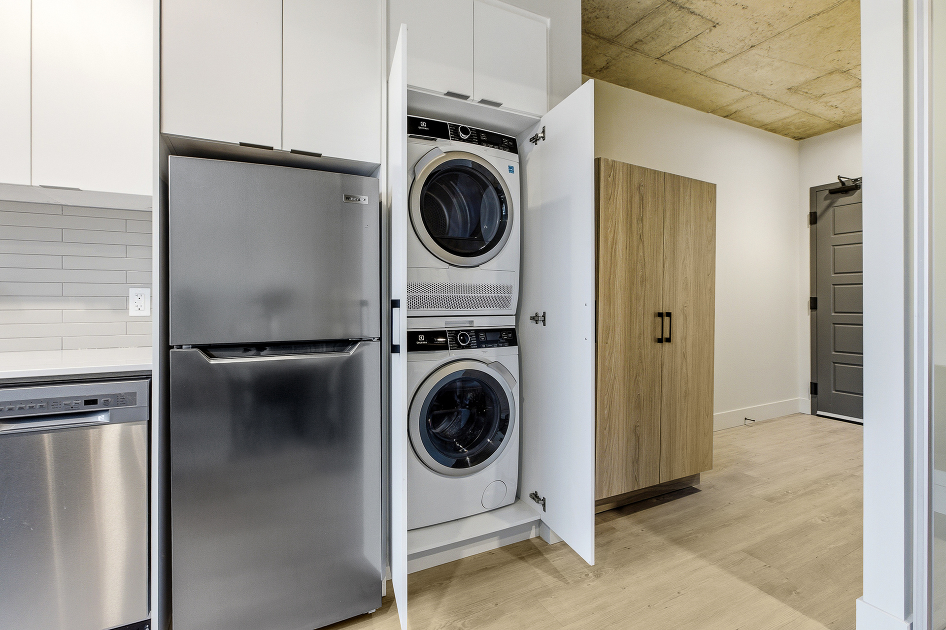 Modern apartment laundry area featuring sleek stainless steel appliances and a convenient stacked washer-dryer tucked behind elegant cabinetry.