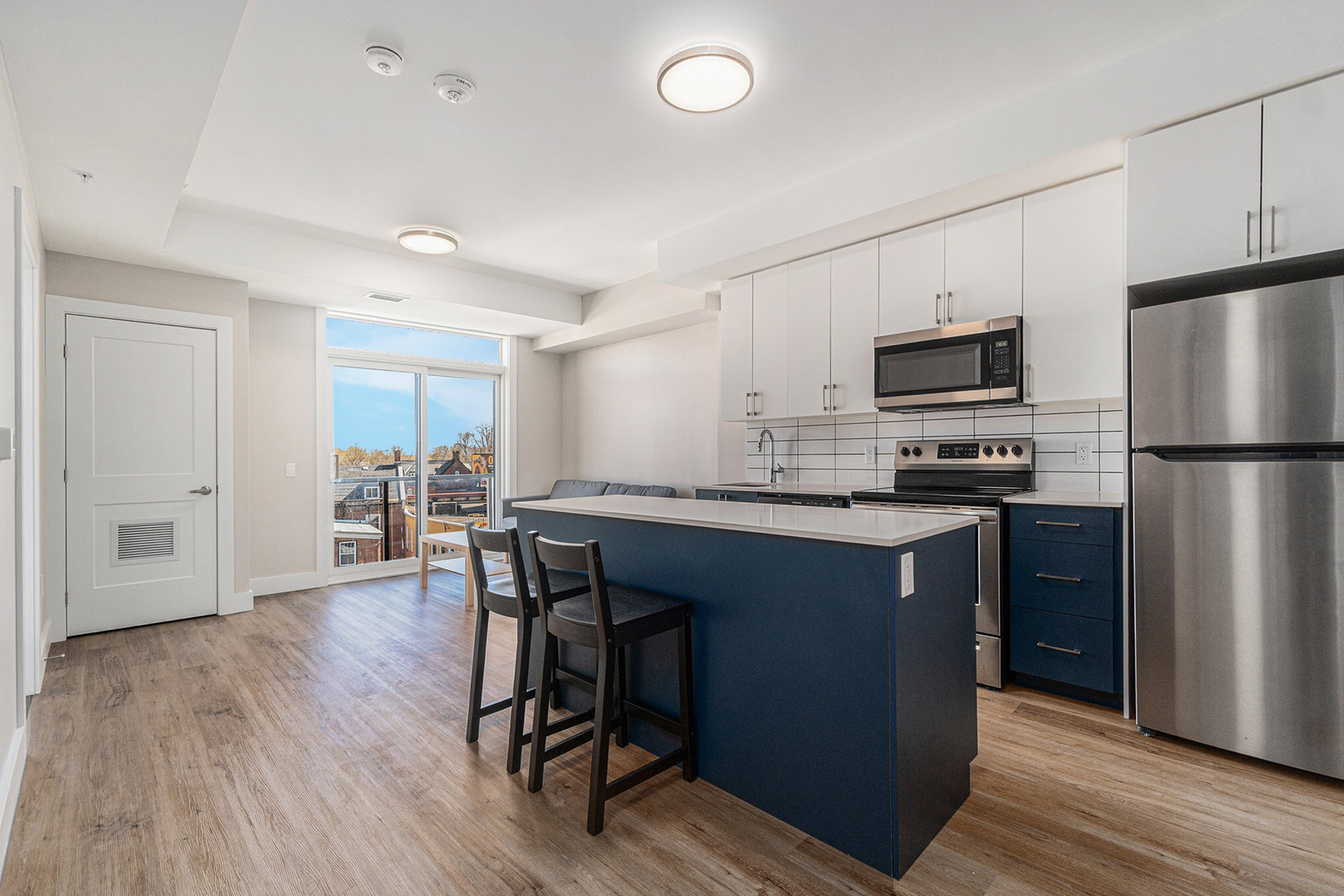Modern apartment kitchen with sleek cabinetry, stainless steel appliances, and a spacious dining area featuring elegant wood flooring, offering a bright and inviting ambiance with a view of the balcony.