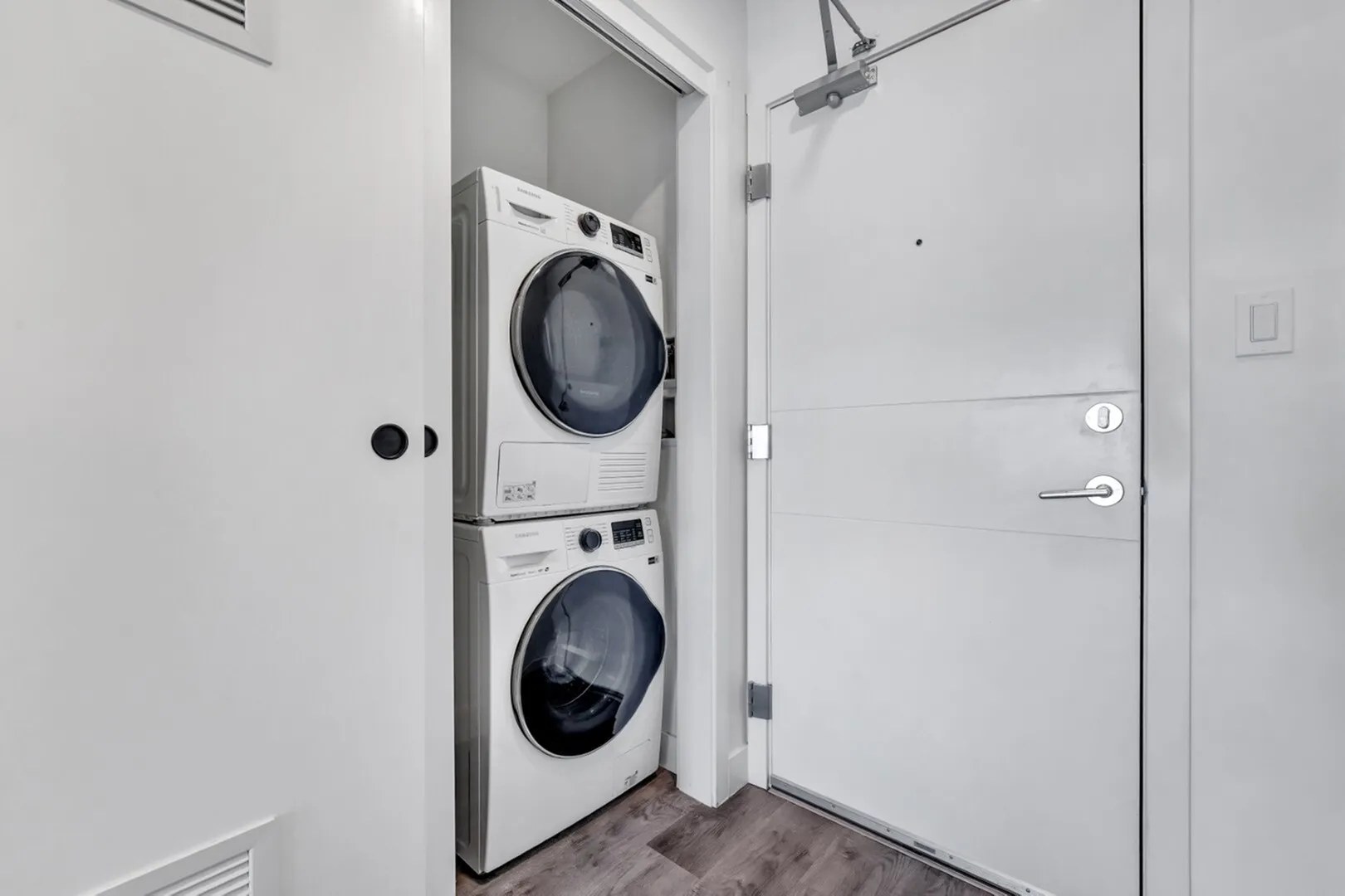 Modern apartment entry with sleek white washing machine and dryer in a compact laundry closet.