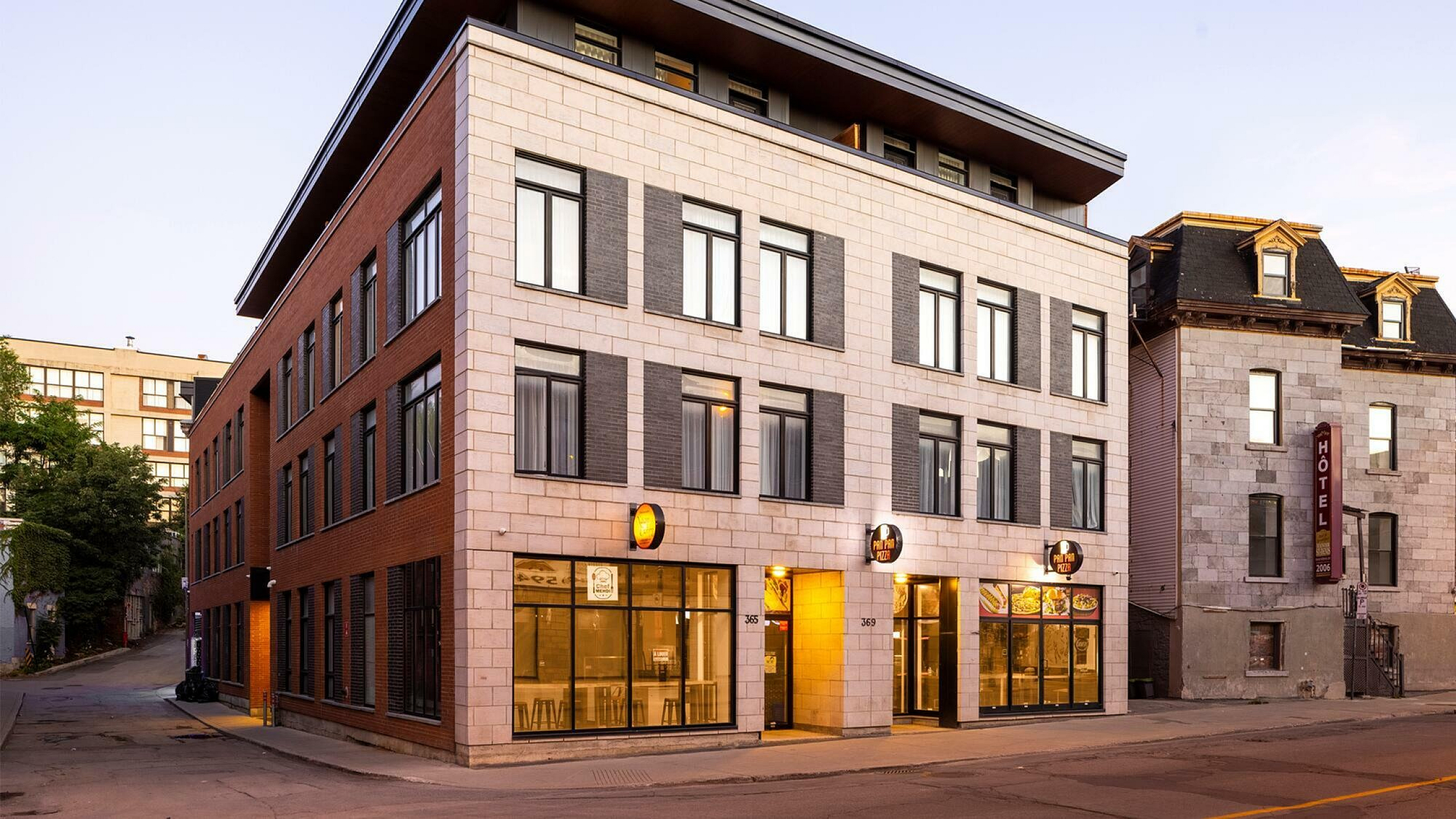 Charming modern building with sleek brick and stone facade, featuring large windows and vibrant street-level eateries.