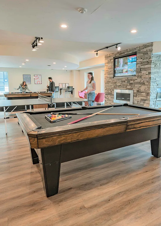 Vibrant recreation room with ping pong and pool tables, modern decor, and ample natural light creating an inviting space for socializing and relaxation.