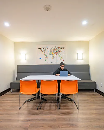 Modern communal workspace with a sleek white table, vibrant orange chairs, and artistic wall map, perfect for productivity and creativity.