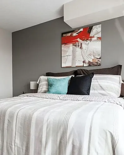 Chic bedroom with modern decor, featuring a cozy bed with colorful cushions, warm wooden flooring, and contemporary wall art.