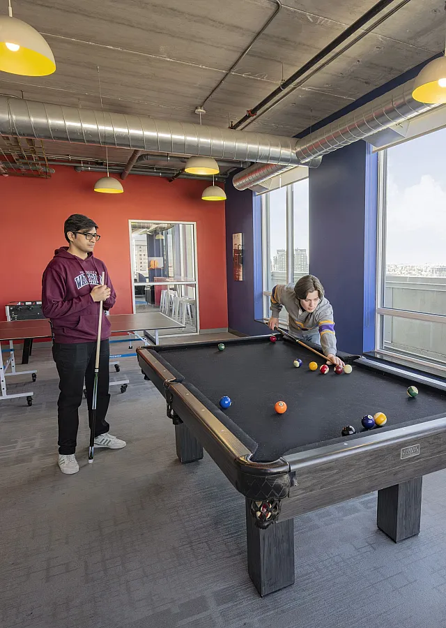 Chic apartment game room with pool table and table tennis, large windows offering stunning city views, and trendy industrial decor.