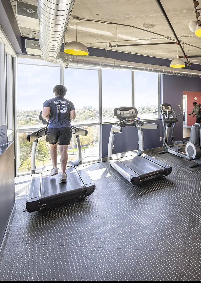 Bright and modern fitness center with panoramic city views, featuring treadmills, weightlifting equipment, and vibrant red and blue decor.