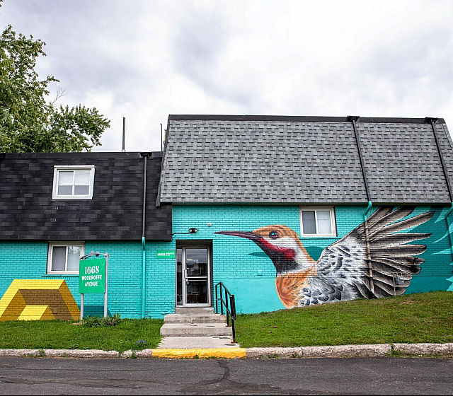 Vibrant turquoise house with eye-catching bird mural, modern shingles, and colorful geometric art at 1668 Woodroffe Avenue.