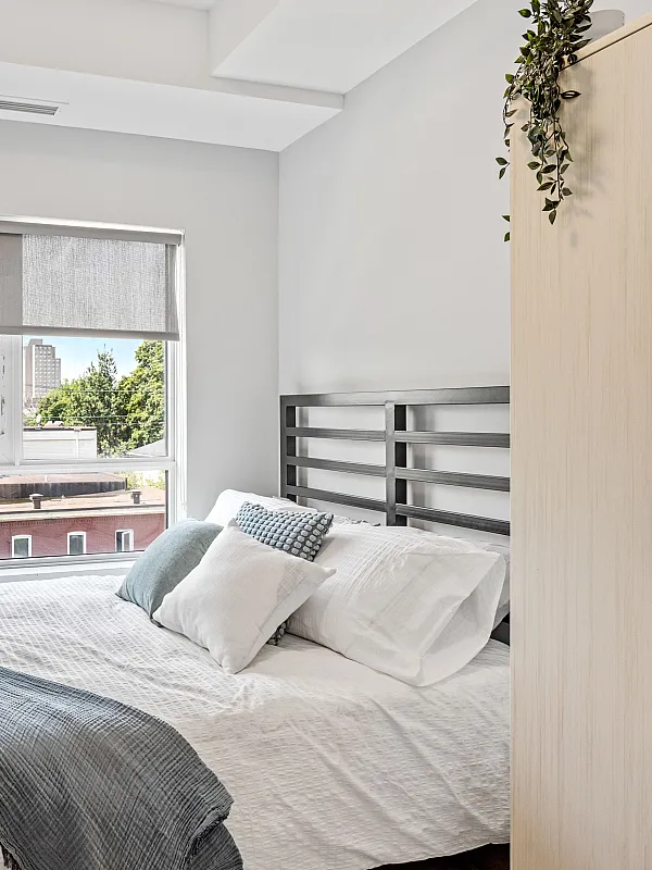 Bright and cozy bedroom with modern decor, featuring a comfortable bed, stylish artwork, and a large window with city views.