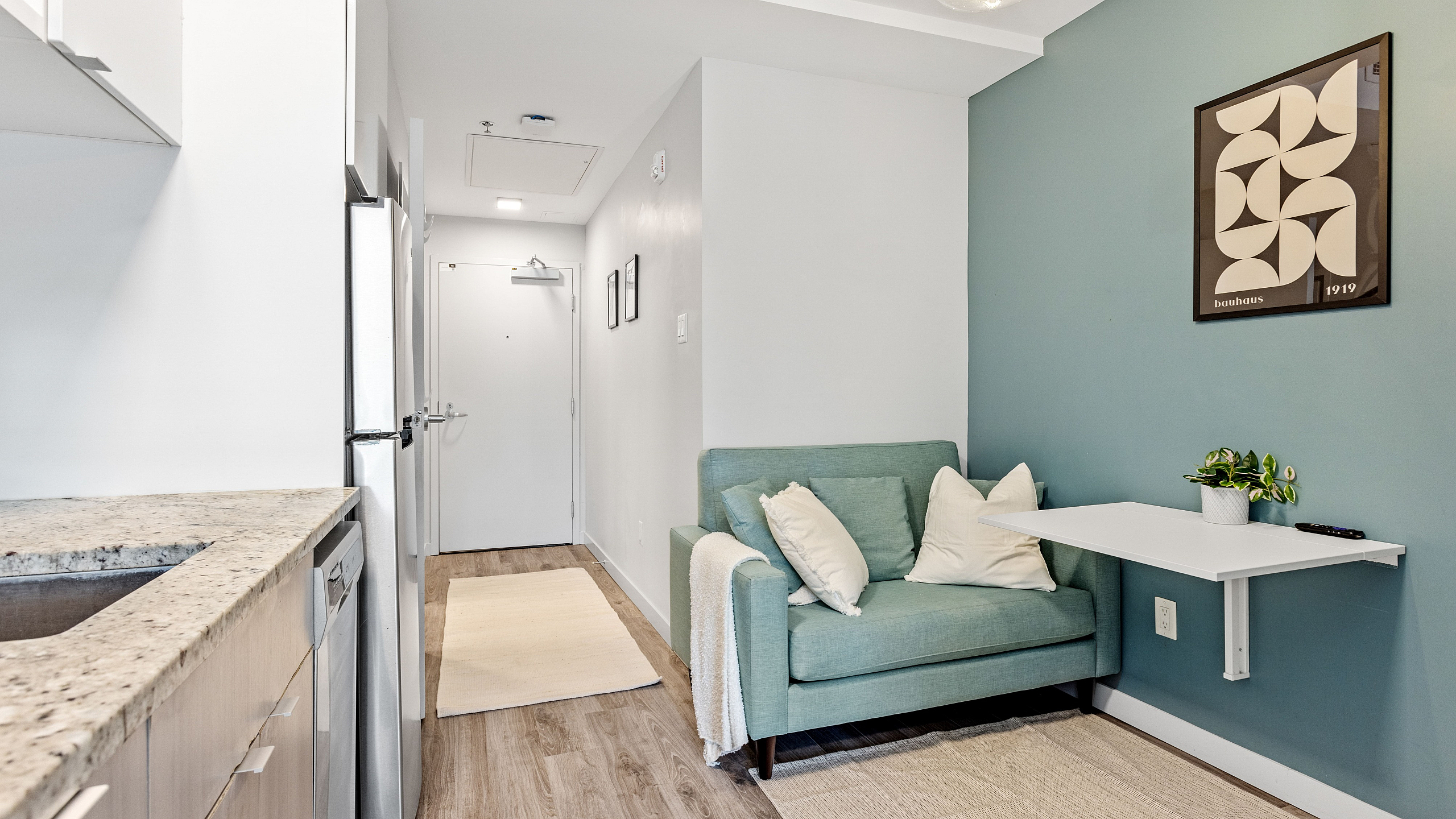 Chic and compact apartment entryway with a cozy teal sofa and sleek fold-down table, perfect for modern living.