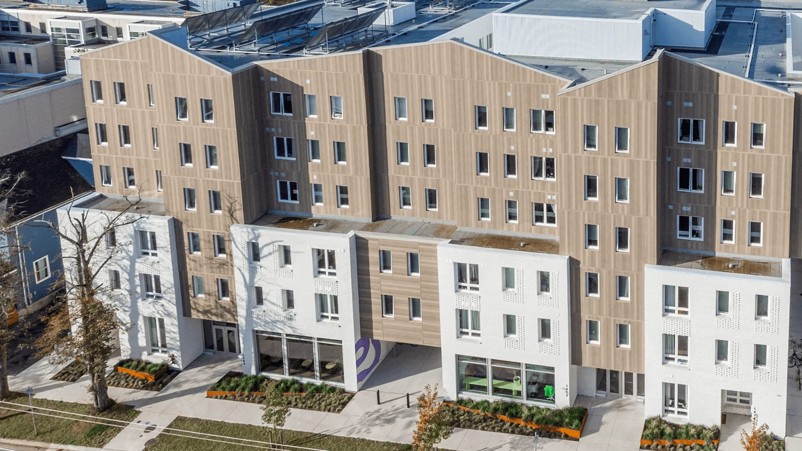 Contemporary apartment building with a unique wooden facade and modern architecture, featuring large windows and lush greenery in a vibrant urban setting.