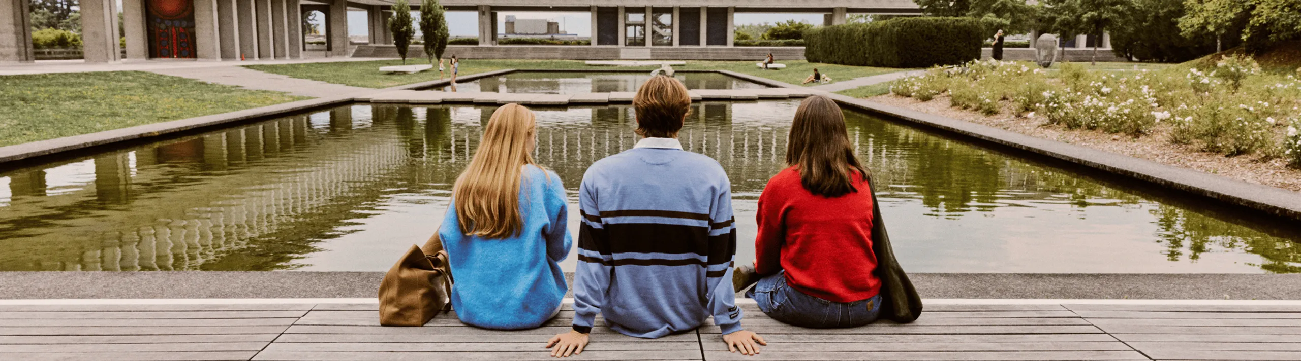Picturesque view of a serene outdoor space with people enjoying the vibrant greenery, tranquil water feature, and modern architecture.