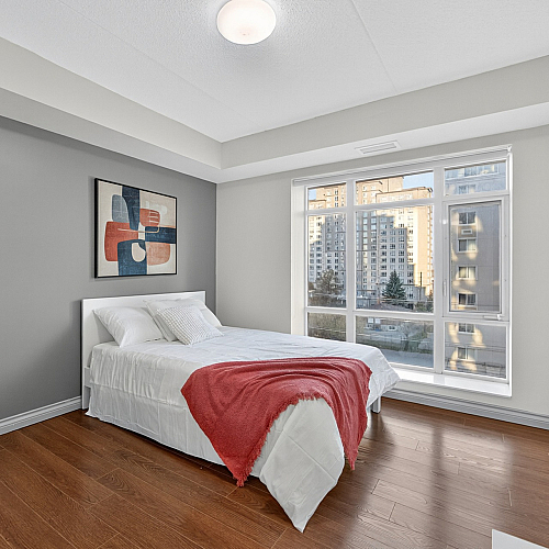 Bright bedroom with large window view, modern artwork, and elegant hardwood flooring in a cozy apartment setting.