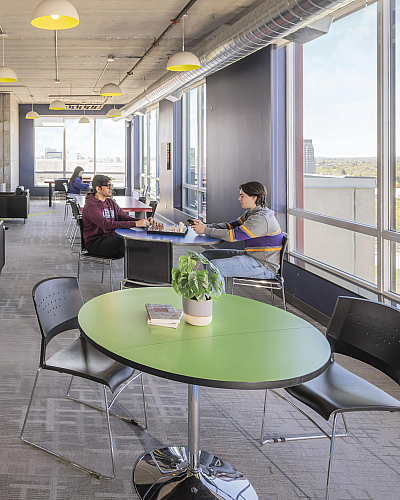 Modern open-concept lounge with stylish black leather seating, large windows with panoramic views, and vibrant green table, creating a welcoming social space.