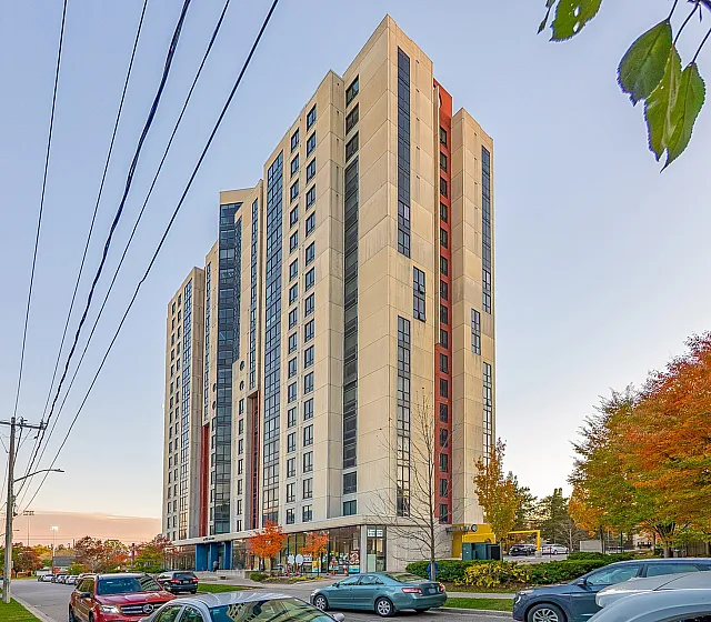 Modern high-rise apartment building set against a clear blue sky, surrounded by vibrant autumn trees and a bustling street.