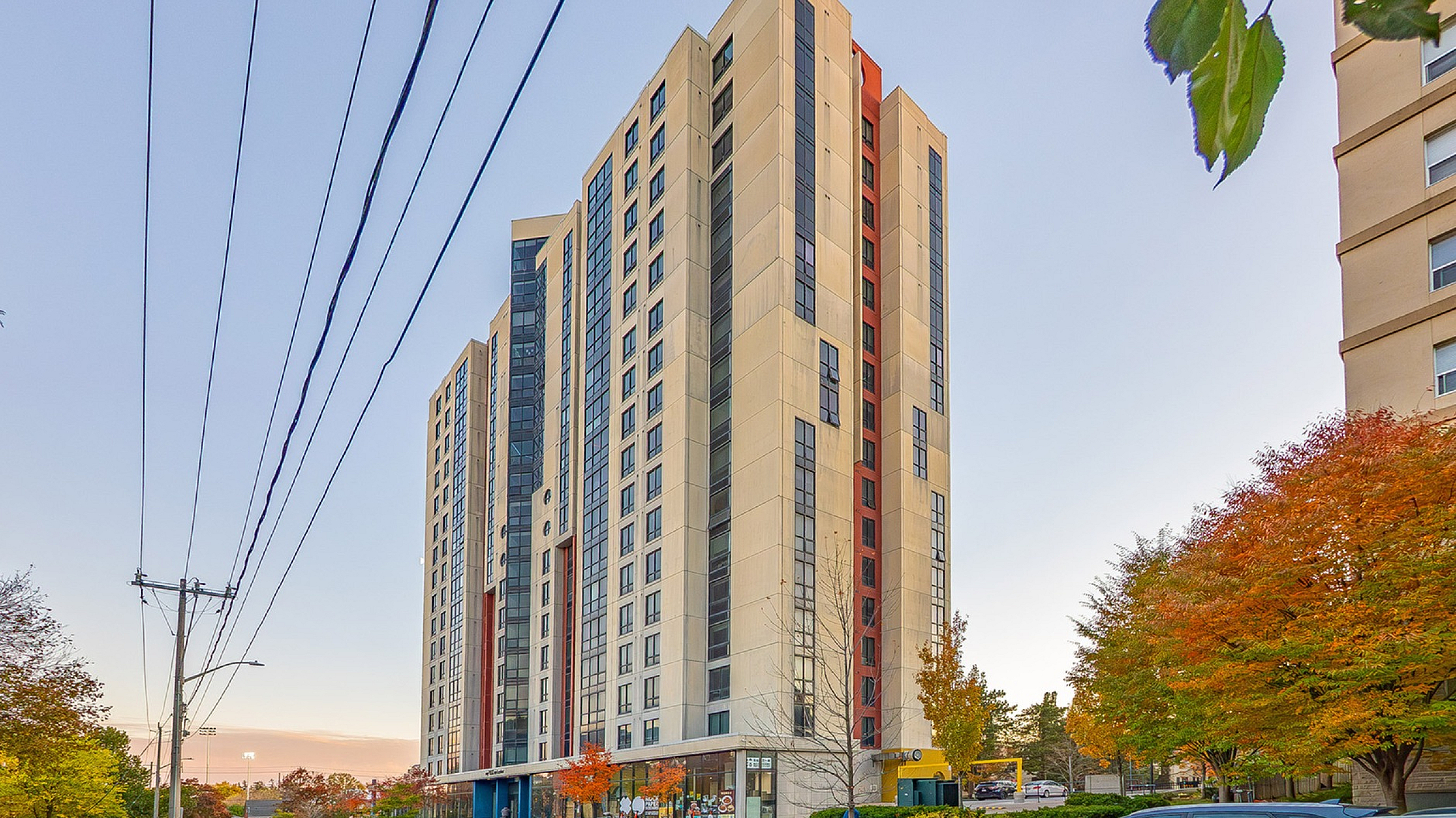 Modern high-rise apartment building with sleek design, surrounded by colorful autumn trees and bustling street in vibrant urban setting.