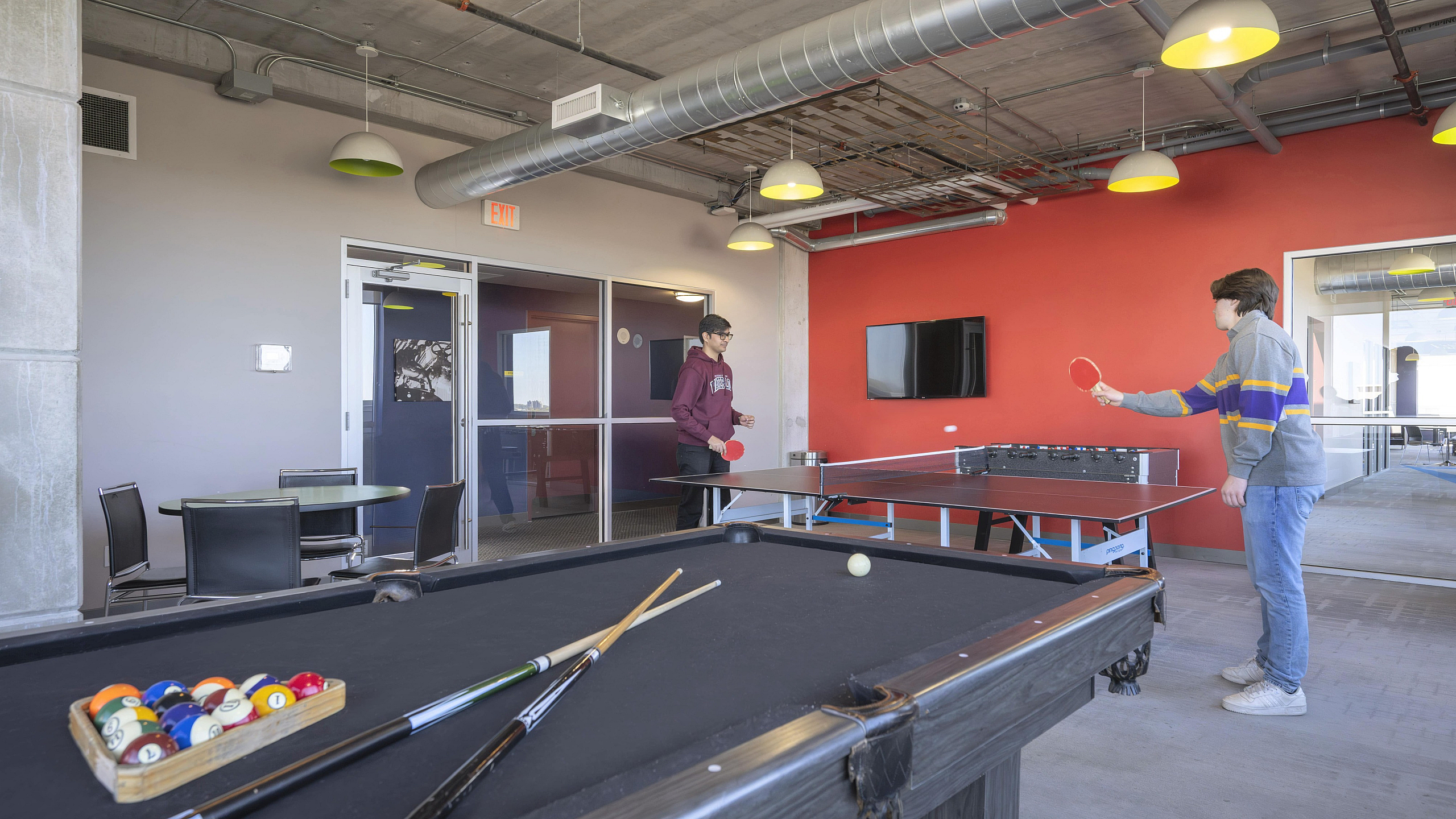 Chic recreational room with a billiards table, vibrant red accent wall, and a lively ping pong match.