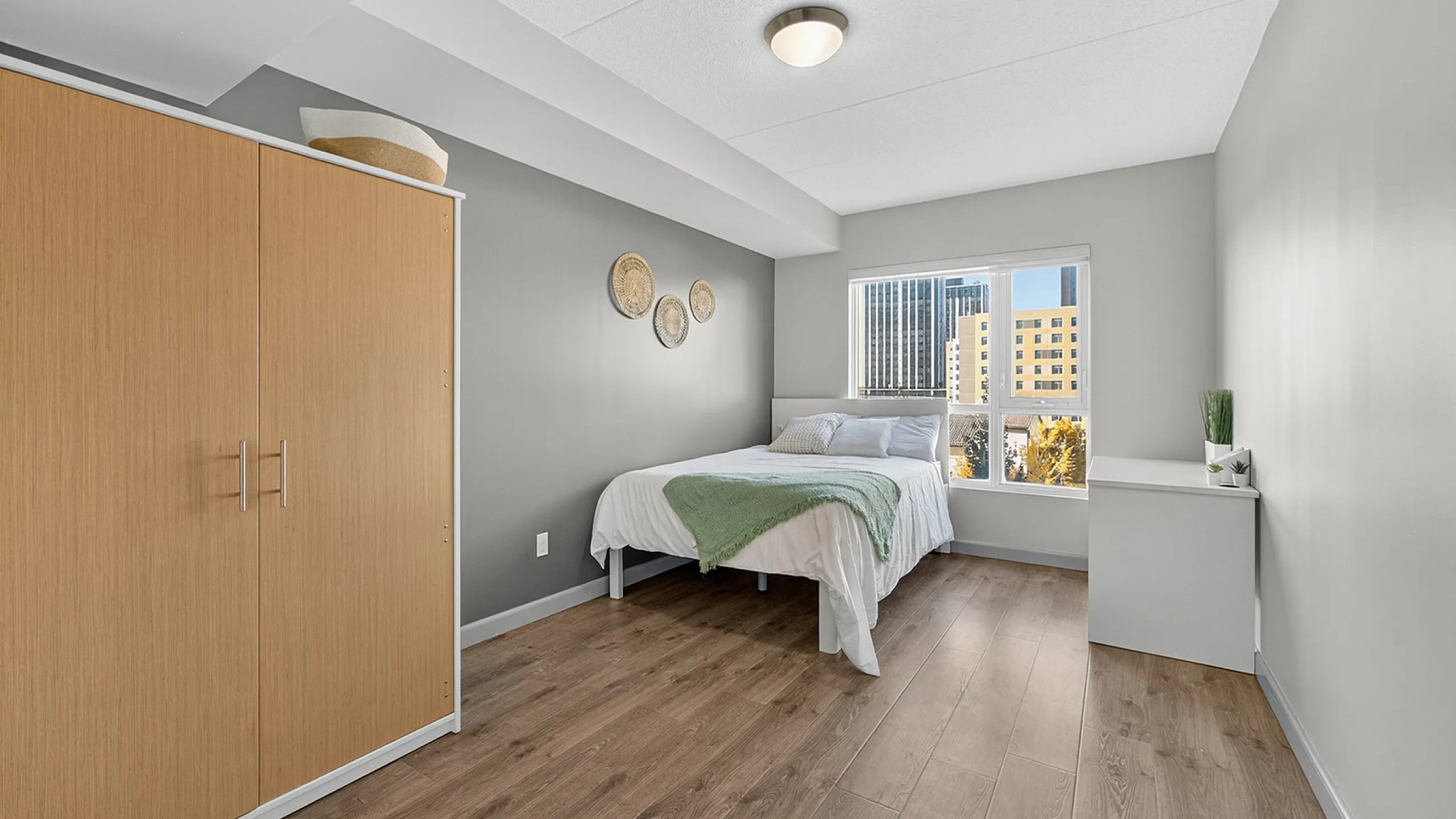 Bright and stylish bedroom featuring wooden flooring, modern decor, and cityscape views through a sunlit window.