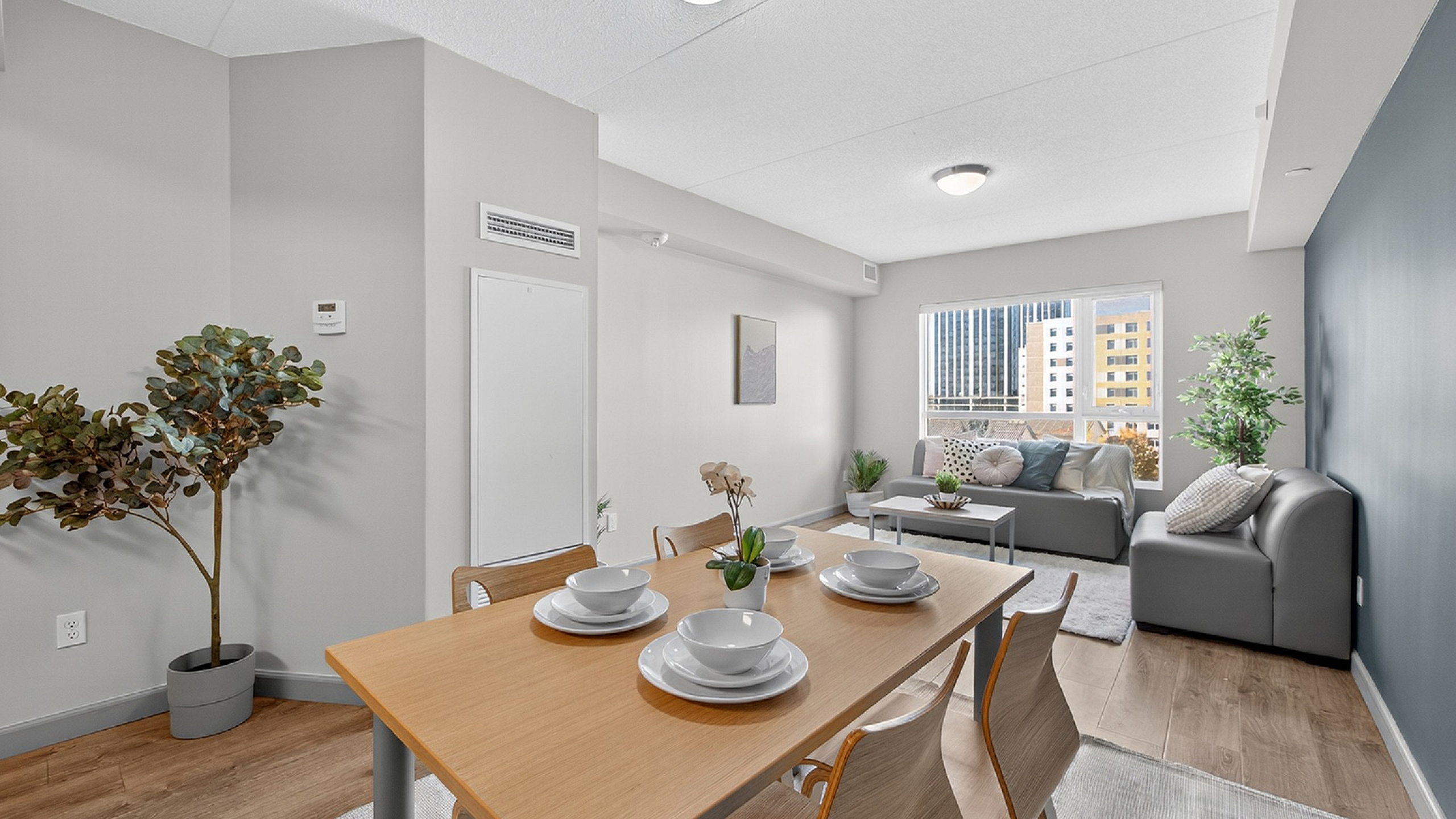 Contemporary open-plan living and dining area with modern furniture and large windows showcasing a vibrant city view.