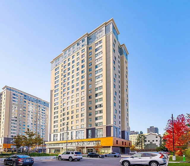 Modern high-rise apartment building under a clear blue sky, framed by vibrant autumn trees.
