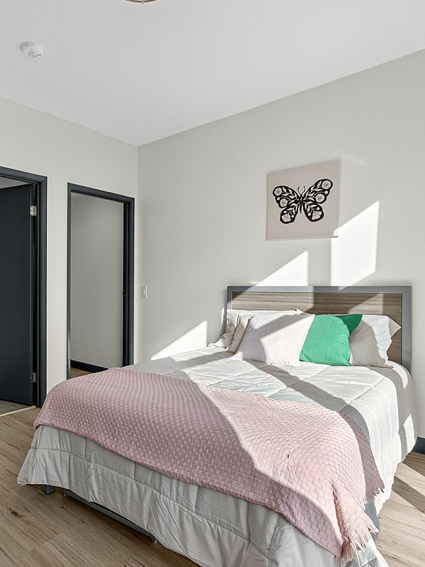 Bright and inviting bedroom with stylish decor, featuring a cozy bed, modern artwork, and sleek wood flooring.