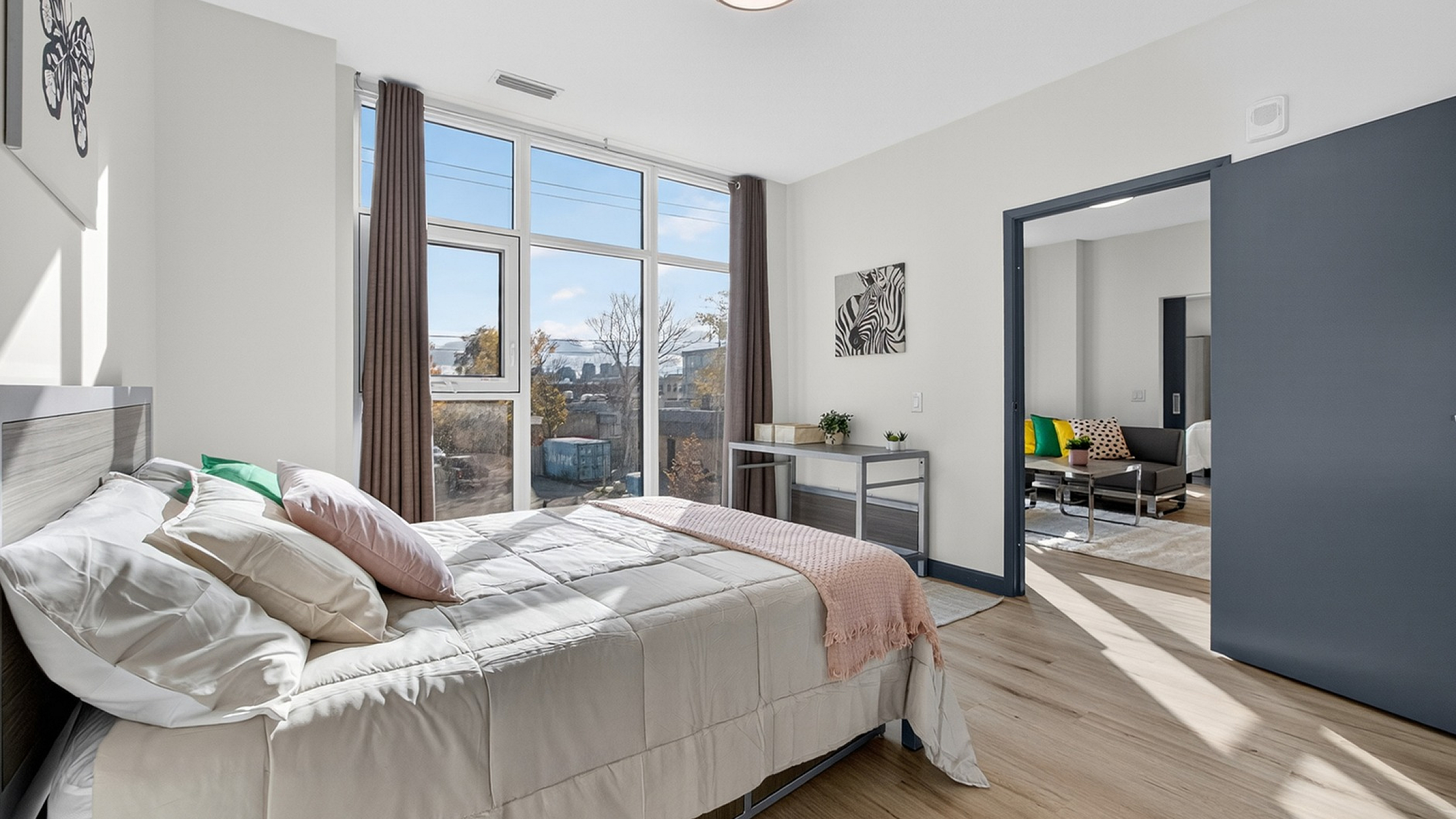 Bright and inviting bedroom featuring floor-to-ceiling windows with panoramic views, modern decor, and seamless access to a cozy living area.