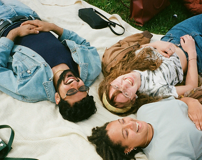 Group of friends laughing and enjoying a sunny day on a cozy picnic blanket in the park.
