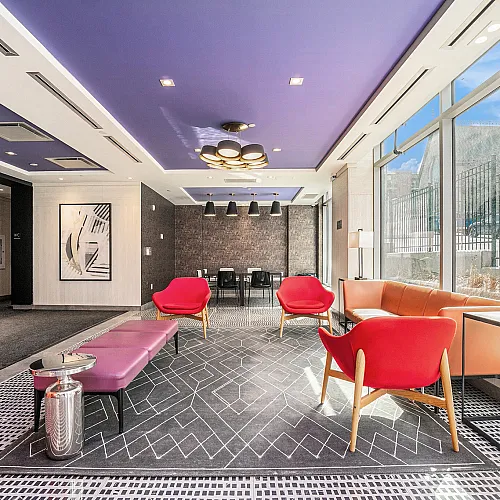 Elegant modern lounge with vibrant red chairs, sleek purple ceiling, and large windows offering abundant natural light.
