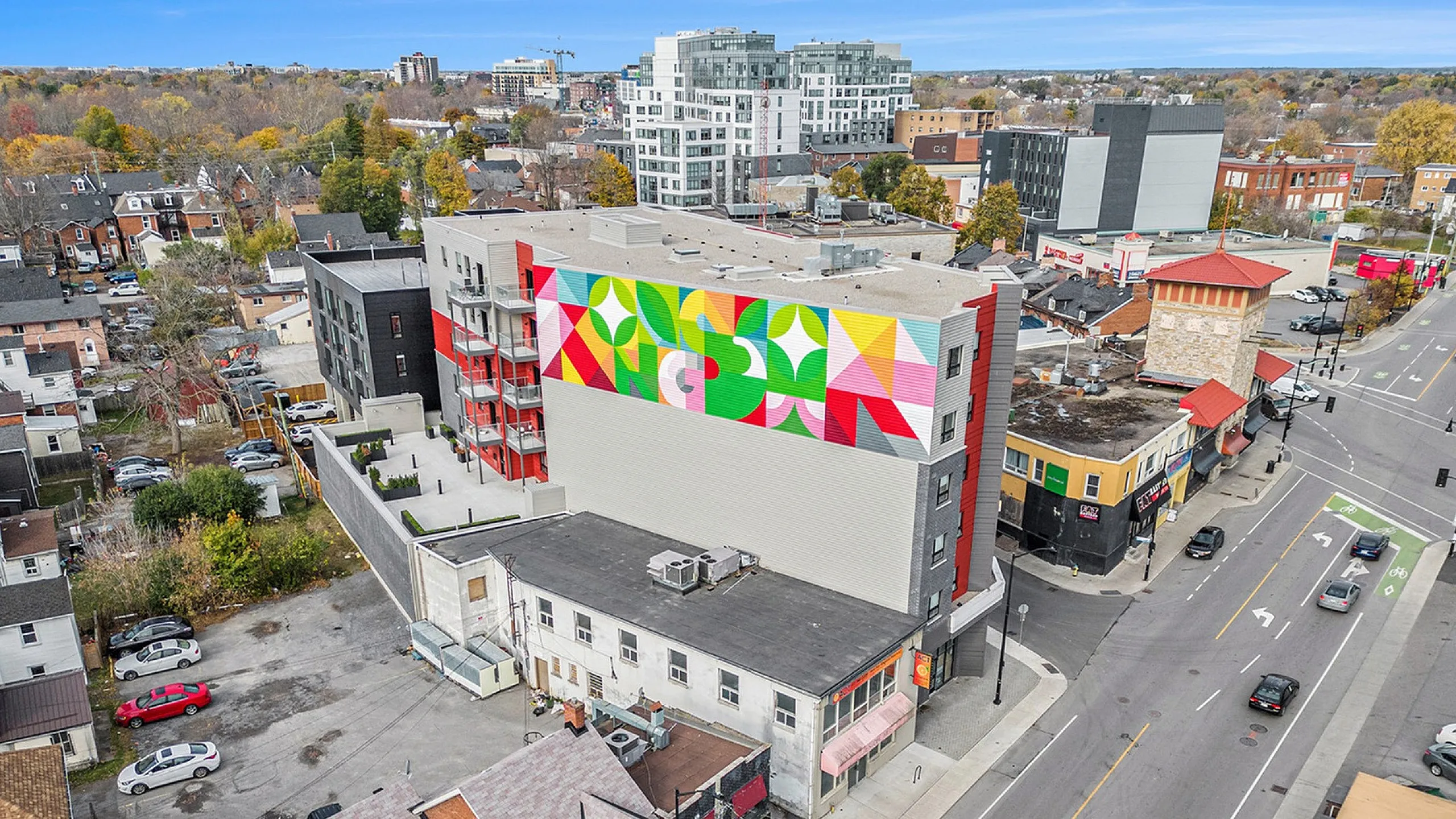Aerial view of vibrant urban neighborhood featuring a colorful mural on a modern apartment building, with charming houses and convenient street access.