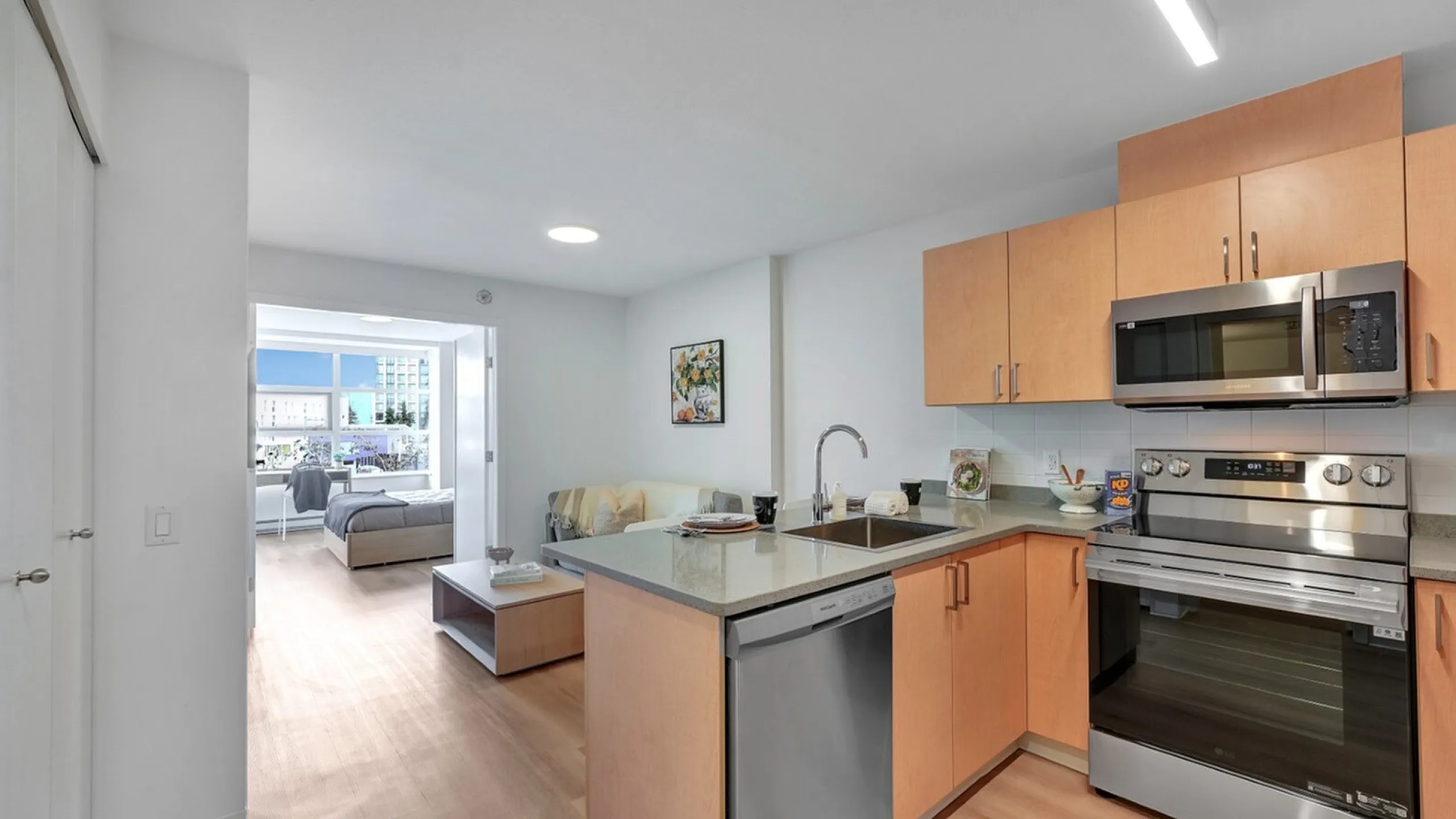 Modern kitchen with sleek stainless steel appliances, open layout leading to a bright living area and spacious bedroom.